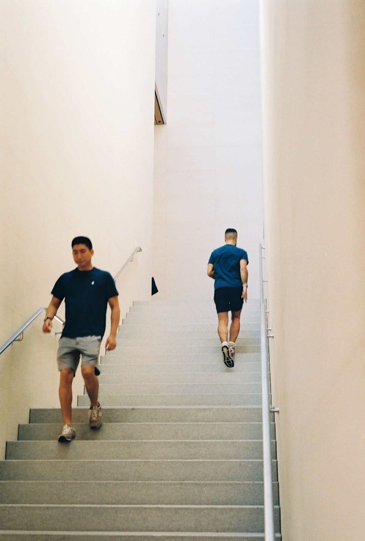 Two people exercising on white stairs in a minimalist interior setting.