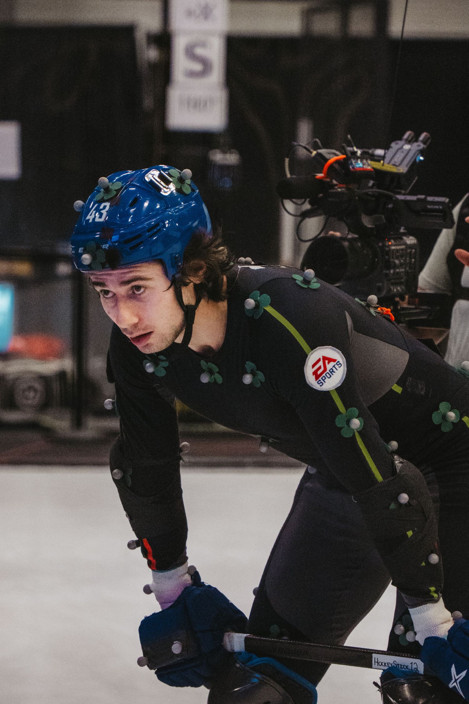 Motion capture performer wearing a blue helmet and black suit with tracking markers in a studio setting.