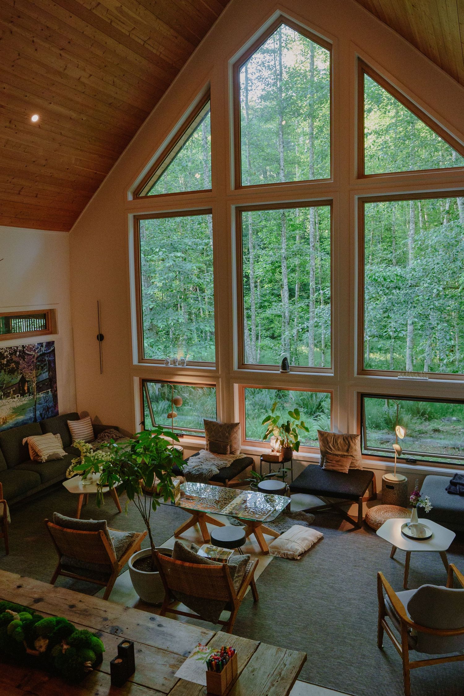 Cozy living room with floor-to-ceiling windows overlooking a lush forest and comfortable seating arrangements.