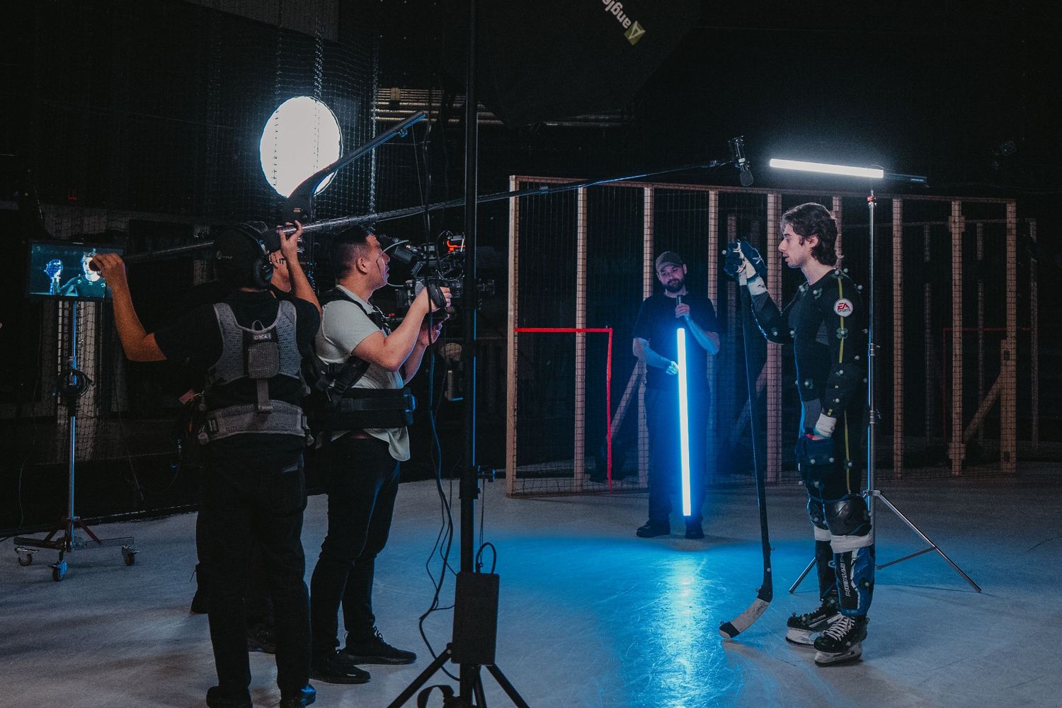 Behind the scenes photo shoot on dark set with blue lighting illumination, video production crew and professional camera setup.
