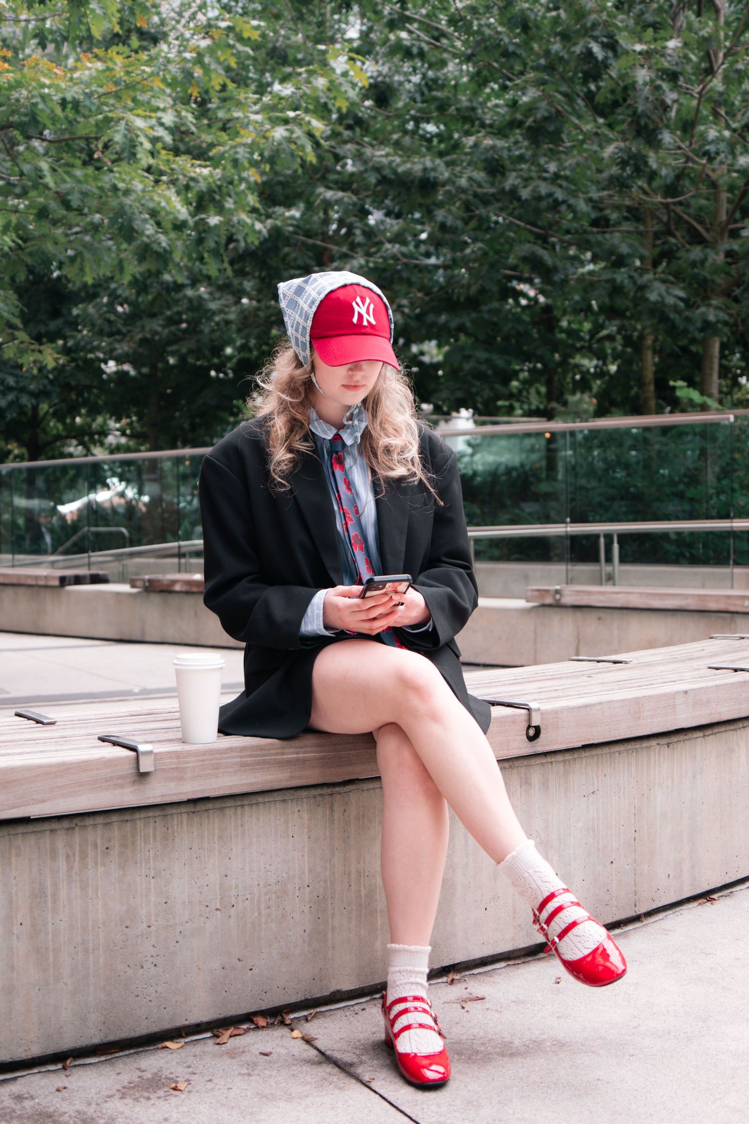Person in dark blazer and red Yankees cap sitting on concrete steps checking phone.