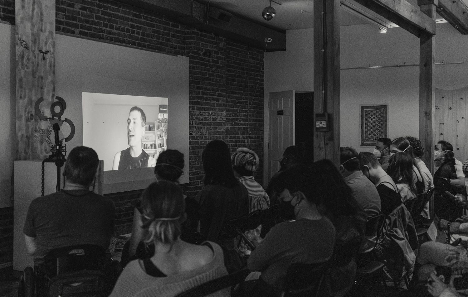 A black and white photo shows people watching a projected presentation in an industrial space.