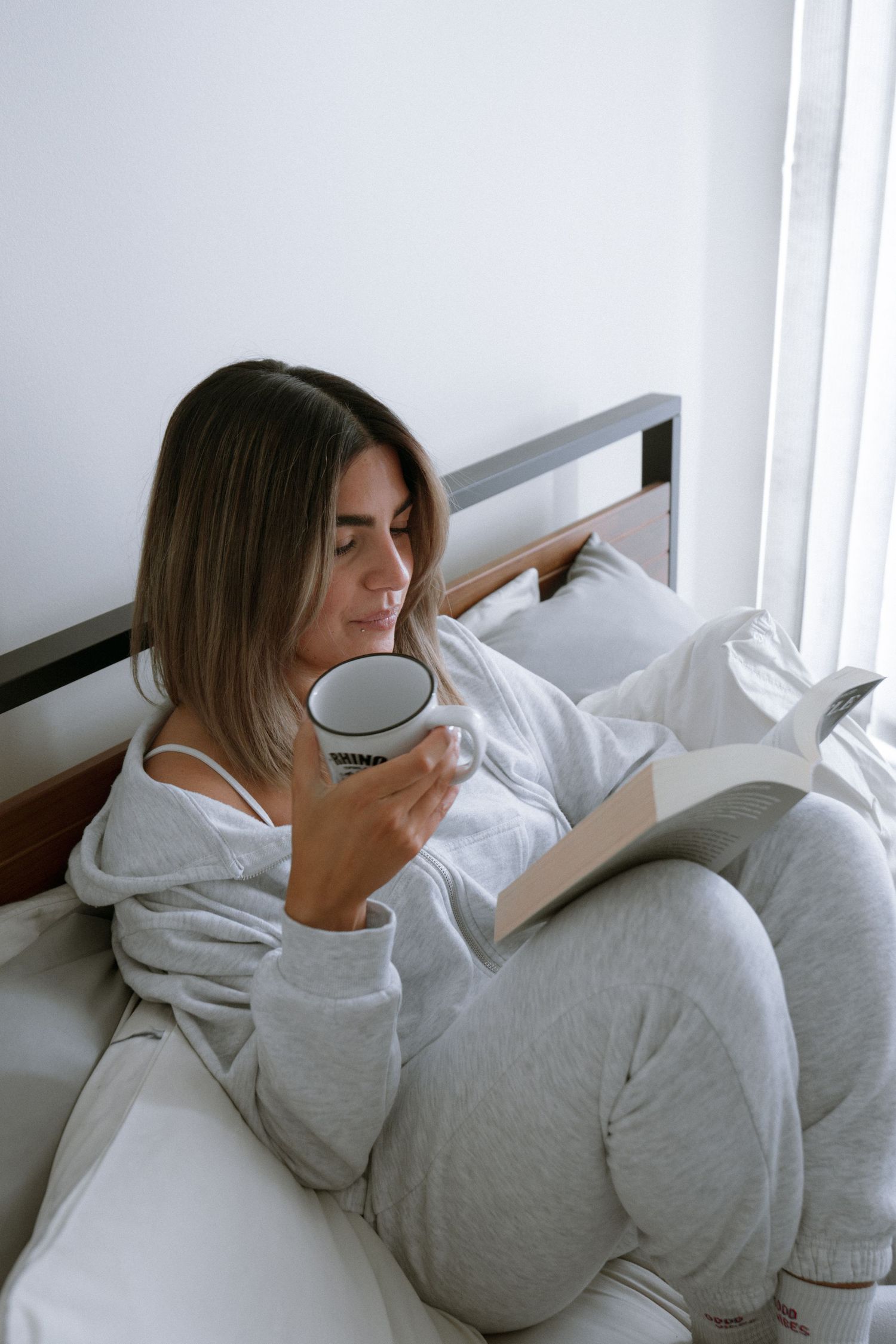 Cozy morning scene with loungewear, coffee cup and book in bed.