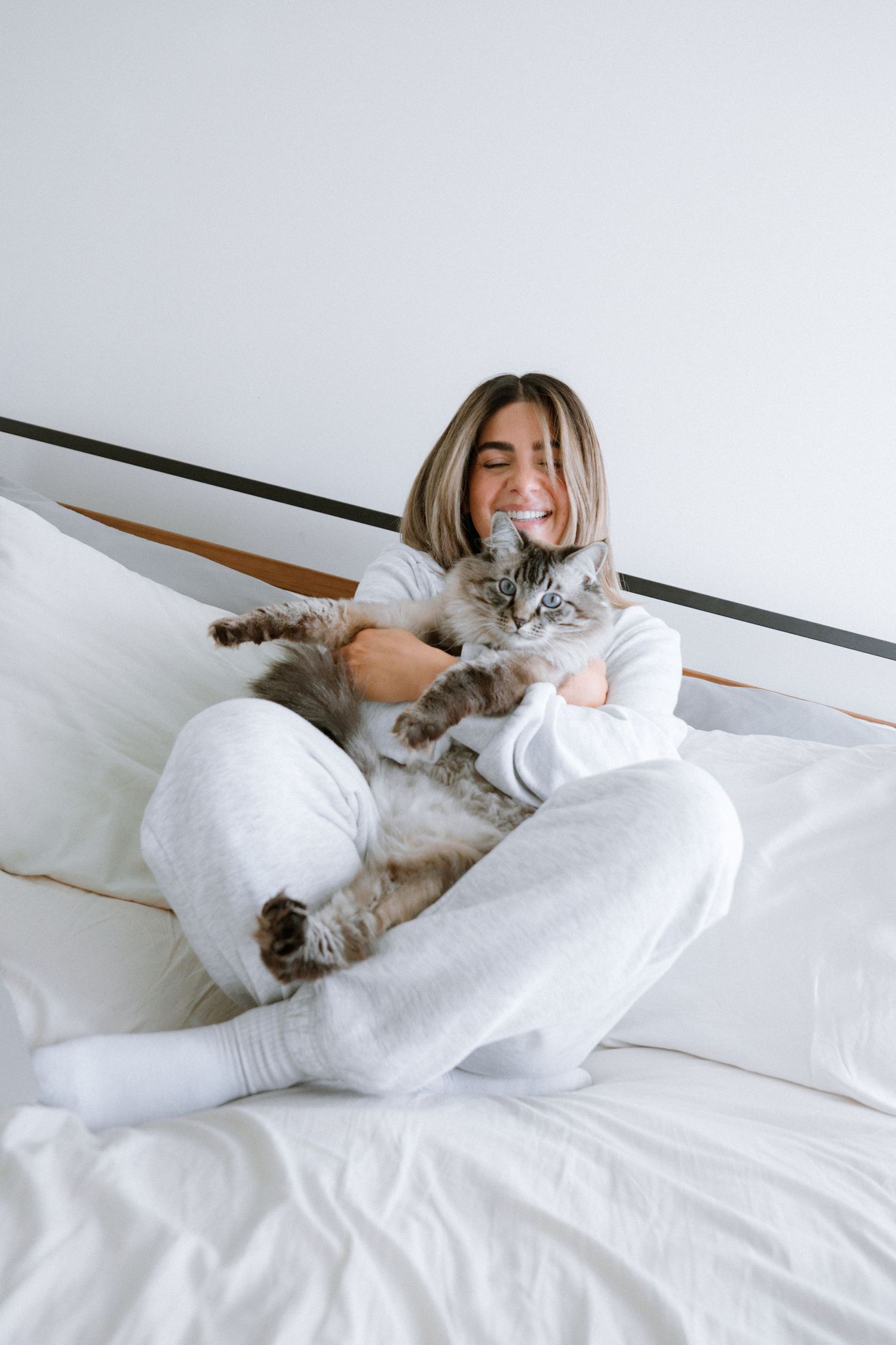 Cozy scene of someone cuddling with a grey cat on white bedding.