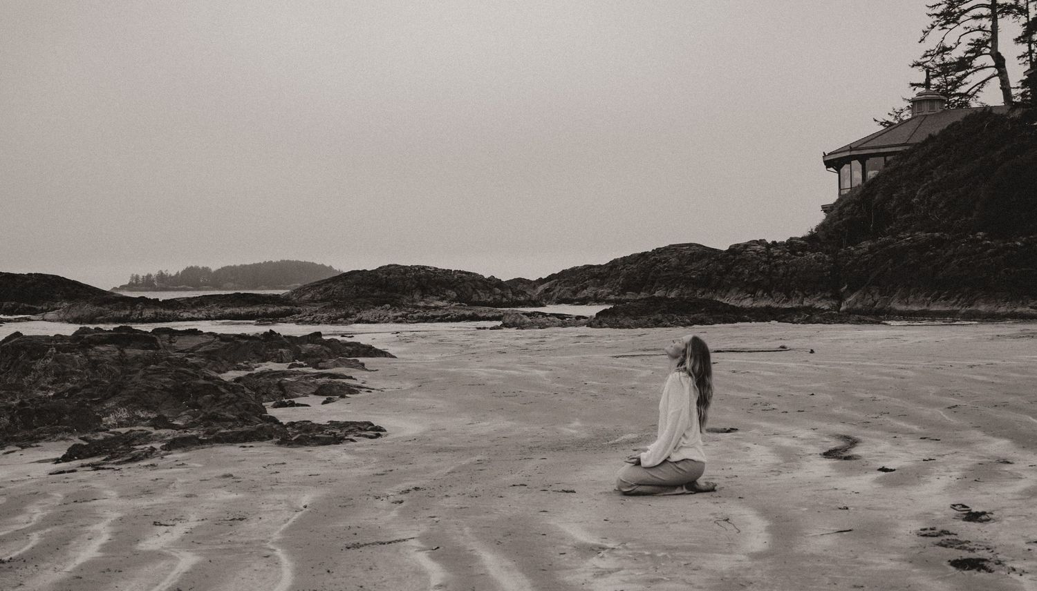 Moody black and white photograph of a lone figure on a rugged Pacific Northwest beach.