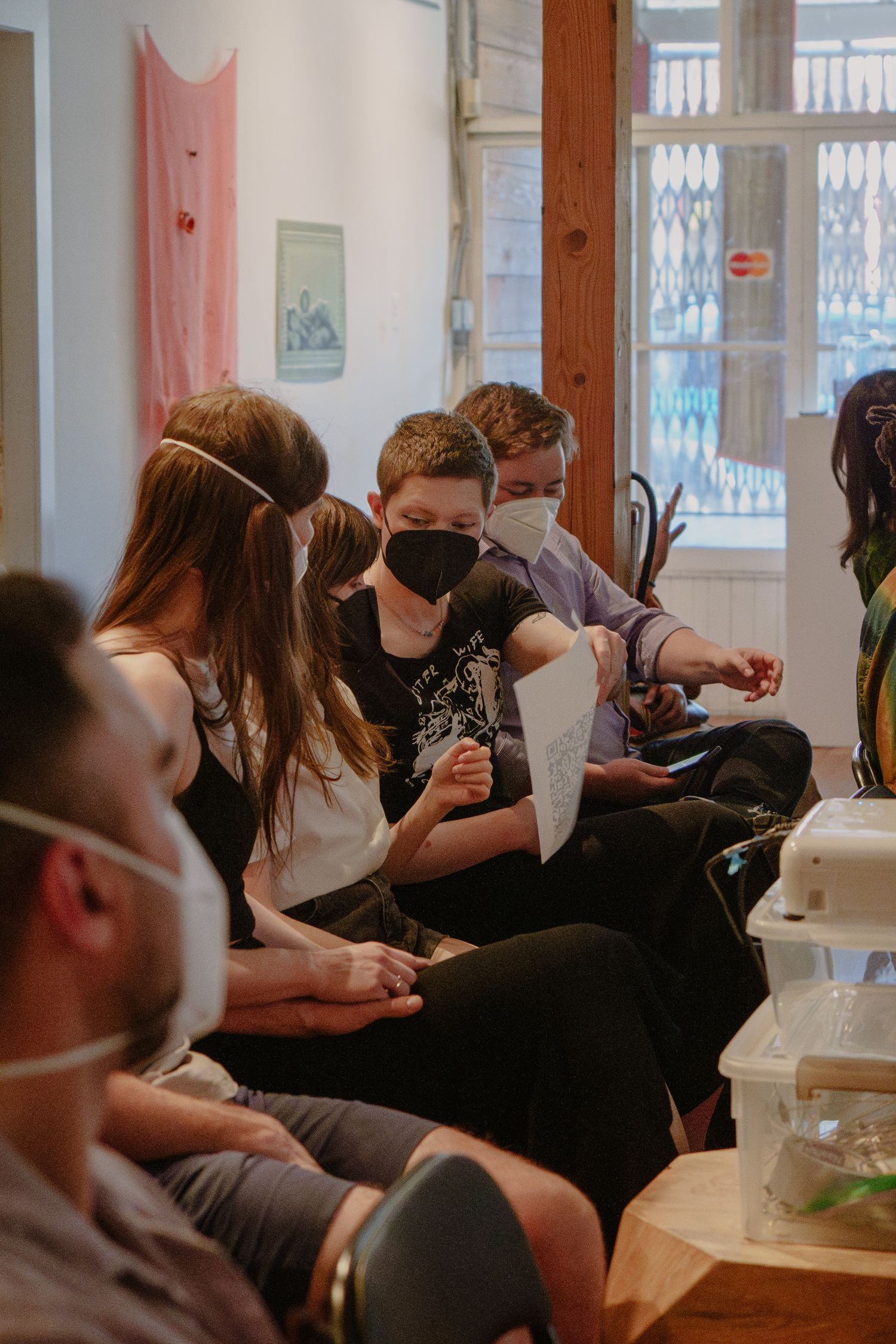 A seated audience wearing masks listens to a presentation in an intimate indoor setting.