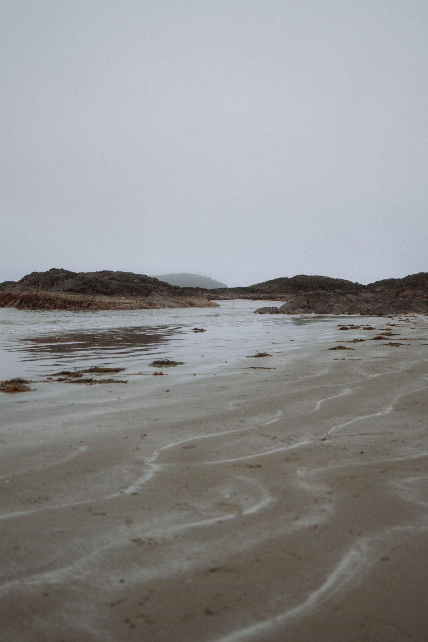 Moody coastal landscape with rocky outcrops and wet sand during low tide.