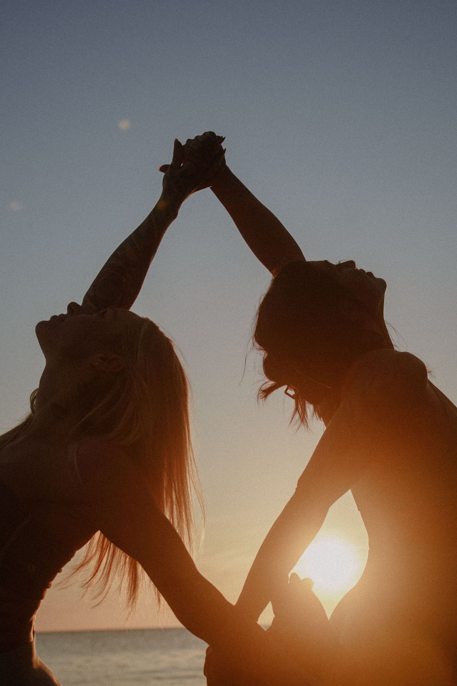 Silhouetted pair dancing together on beach during sunset with joined hands raised.