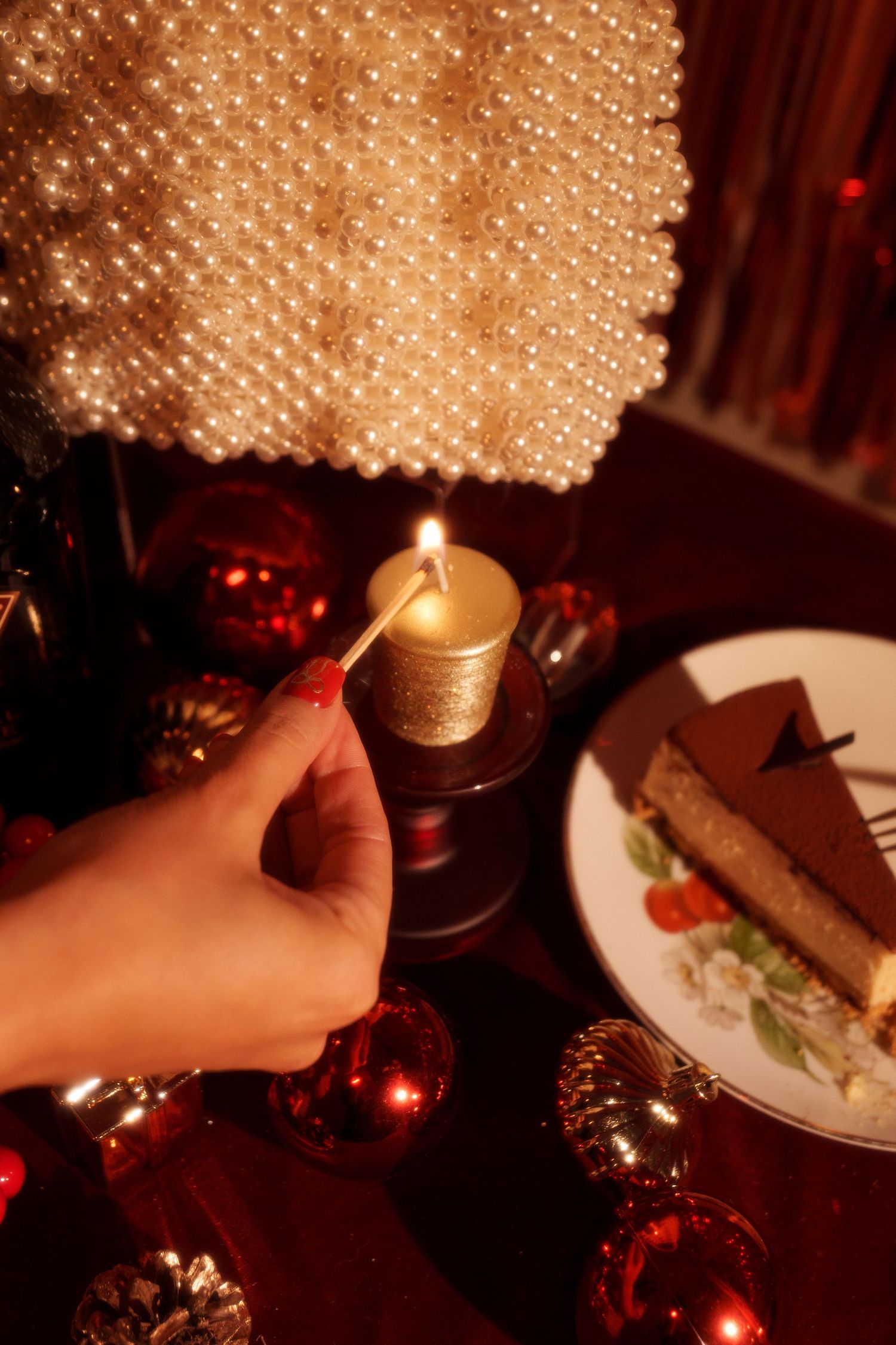Hand lighting a golden candle beside a slice of cake with sparkly holiday decorations.