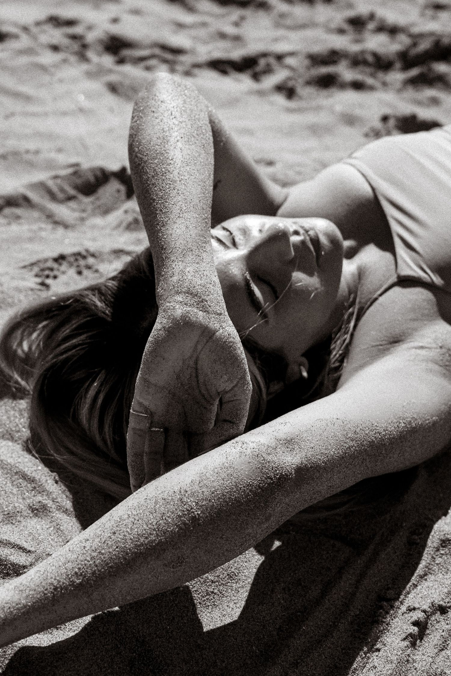 Black and white portrait of person lying in sand at beach.