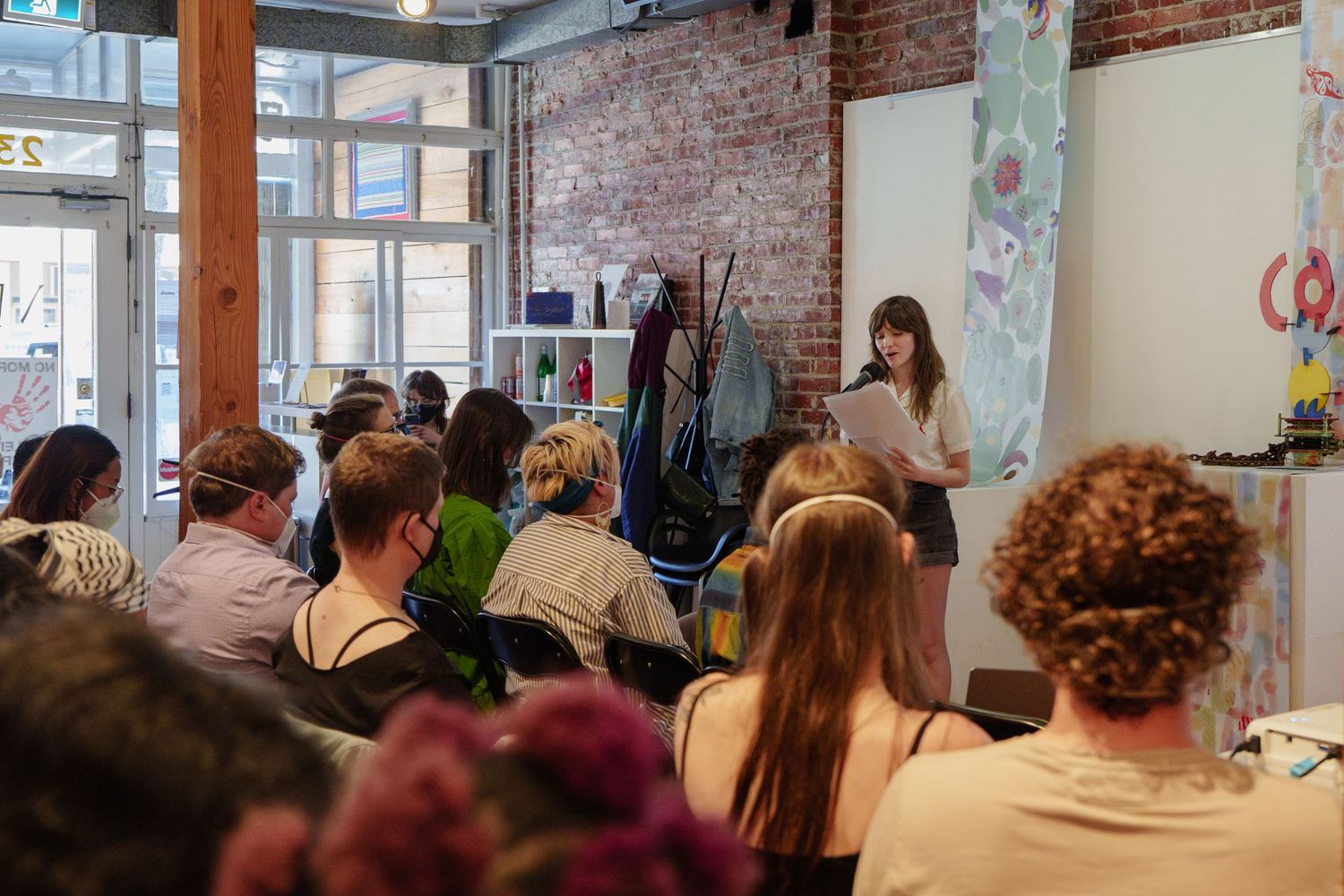 Crowd gathered in bright room with exposed brick walls for presentation.