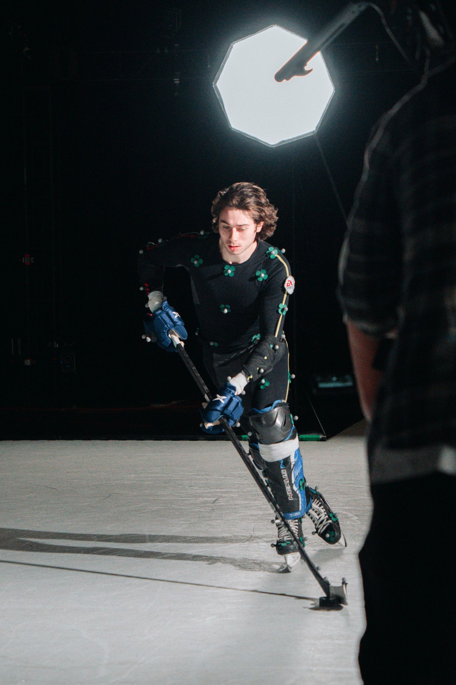Motion capture actor in a black suit performs action moves under dramatic studio lighting.