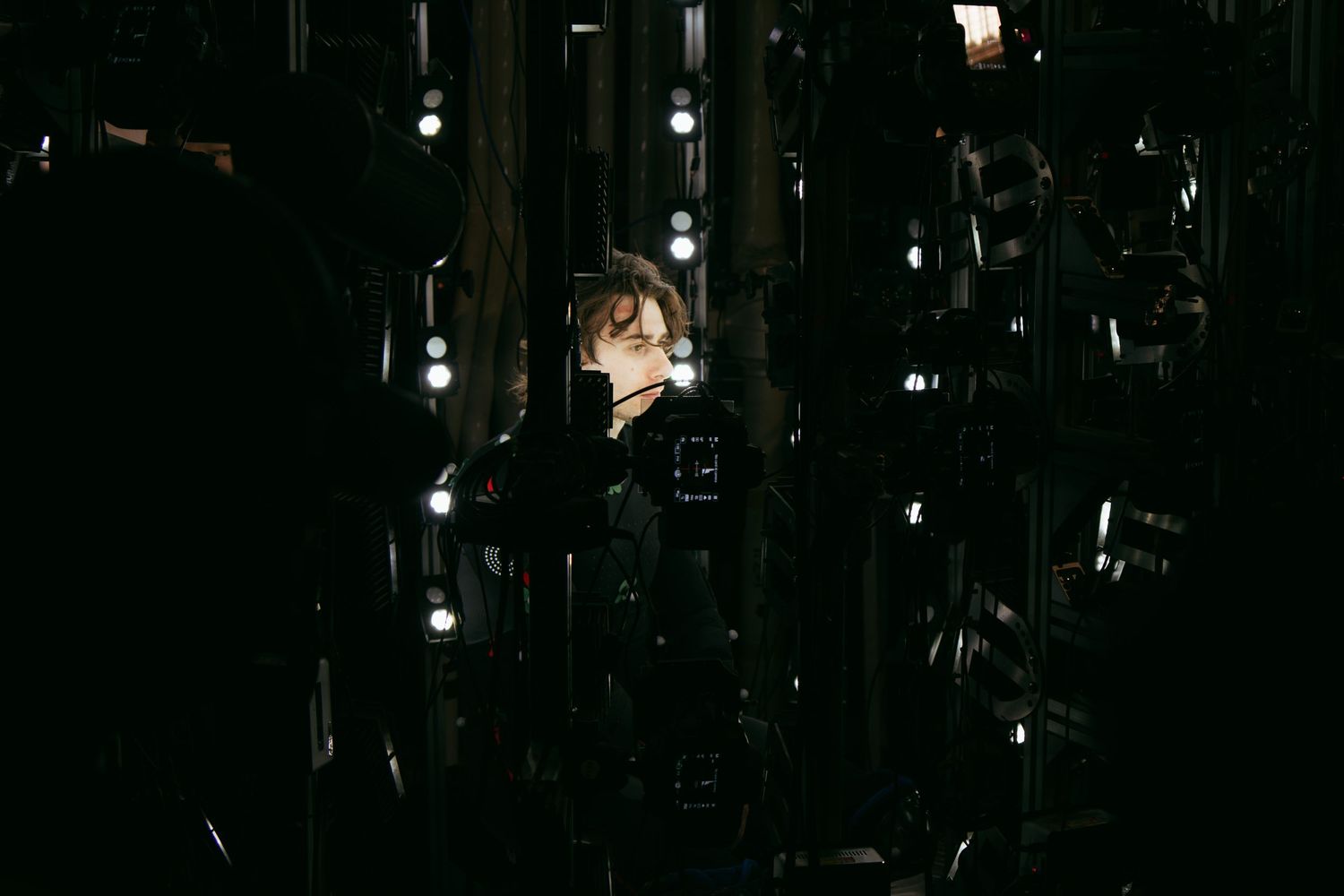 Performer in dark motion capture suit standing against black background with studio lights.