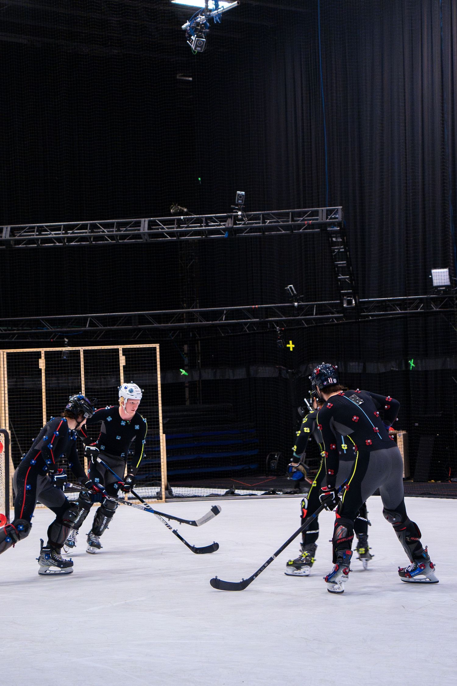 Hockey players in motion capture suits practice on an indoor rink during a filming session.