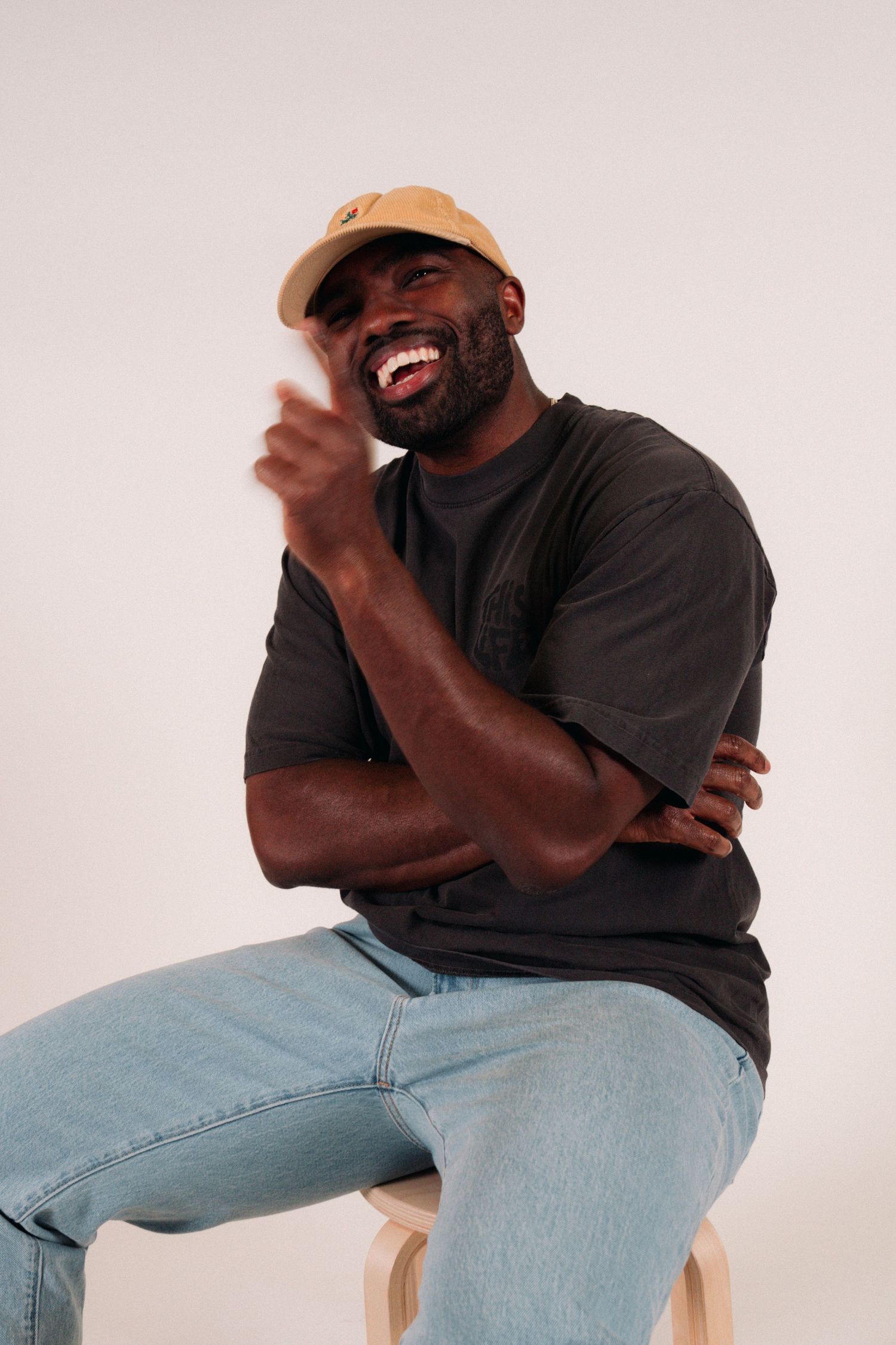 Person in tan cap and dark shirt laughs joyfully while sitting on wooden stool.