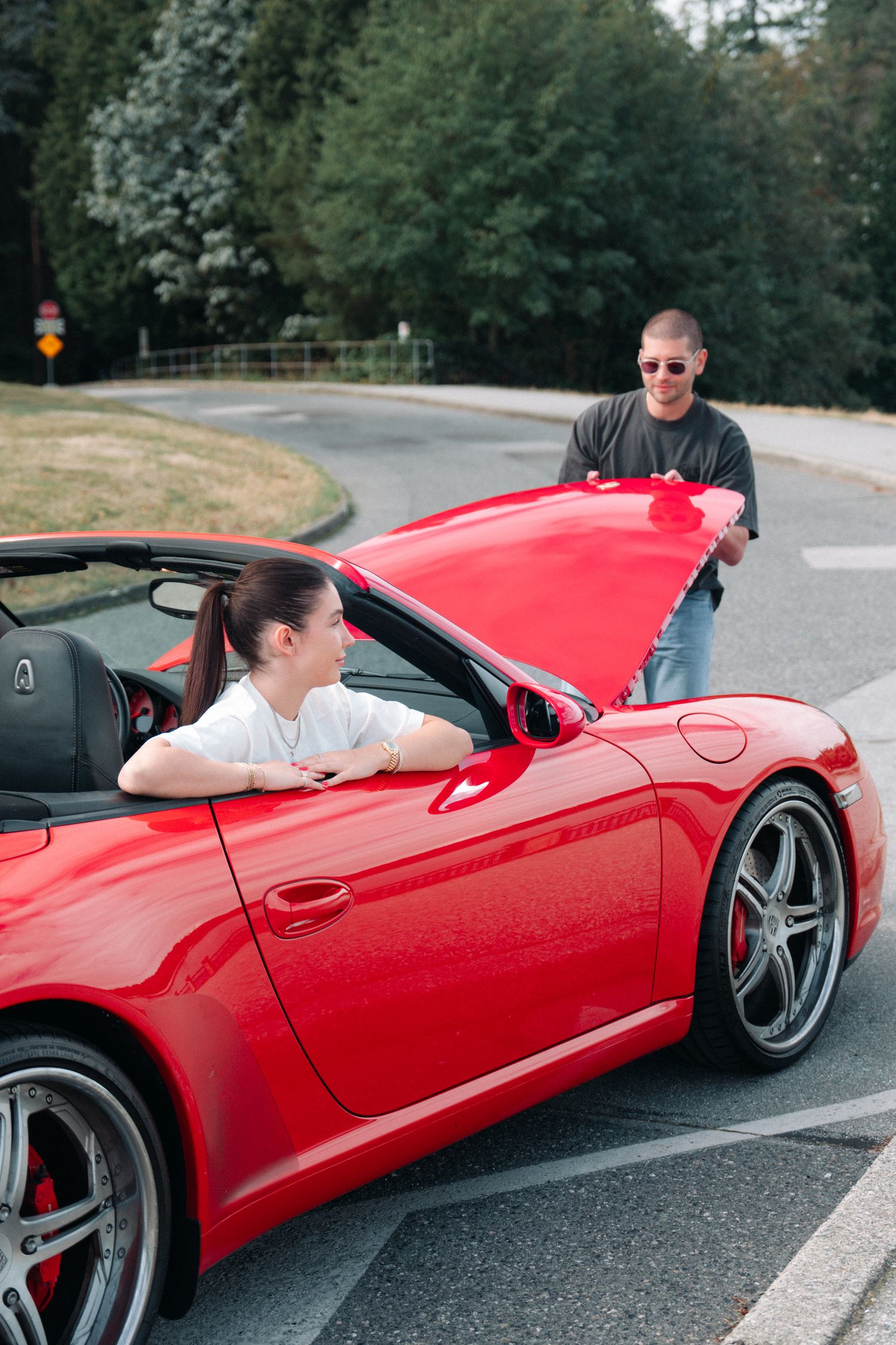 A red Porsche convertible parked on a curved road surrounded by trees.