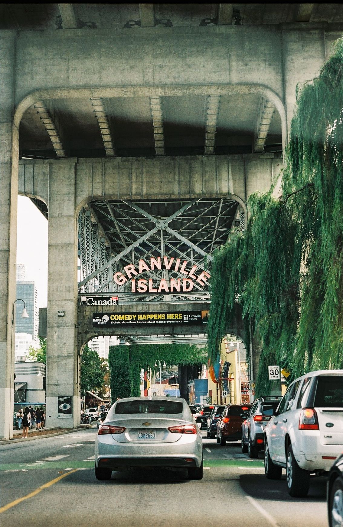Granville Island entrance sign under bridge with cars waiting to enter.