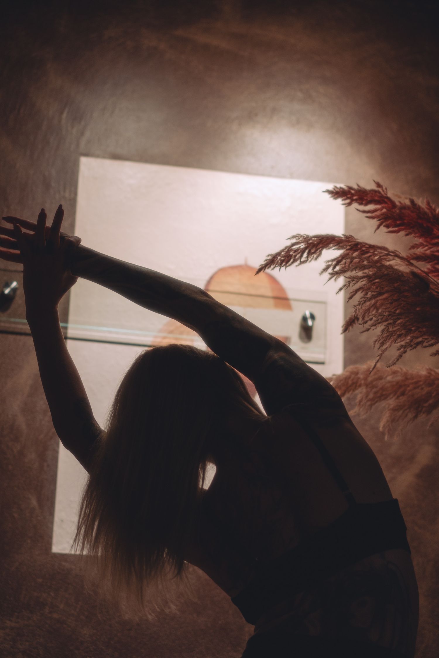 Dramatic silhouette poses against sunset window with decorative pampas grass.