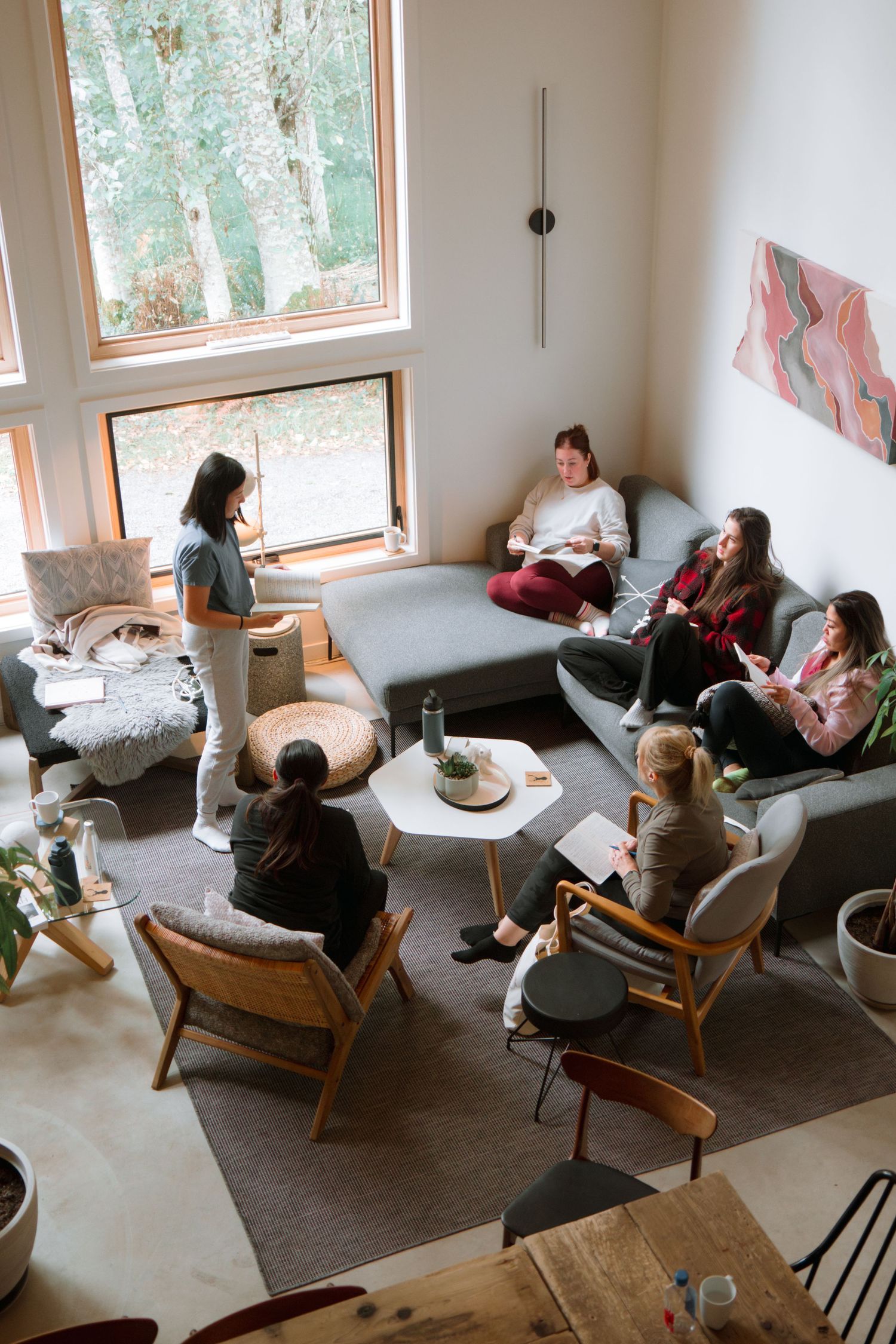 Cozy living room gathering with modern furniture and large windows overlooking nature.