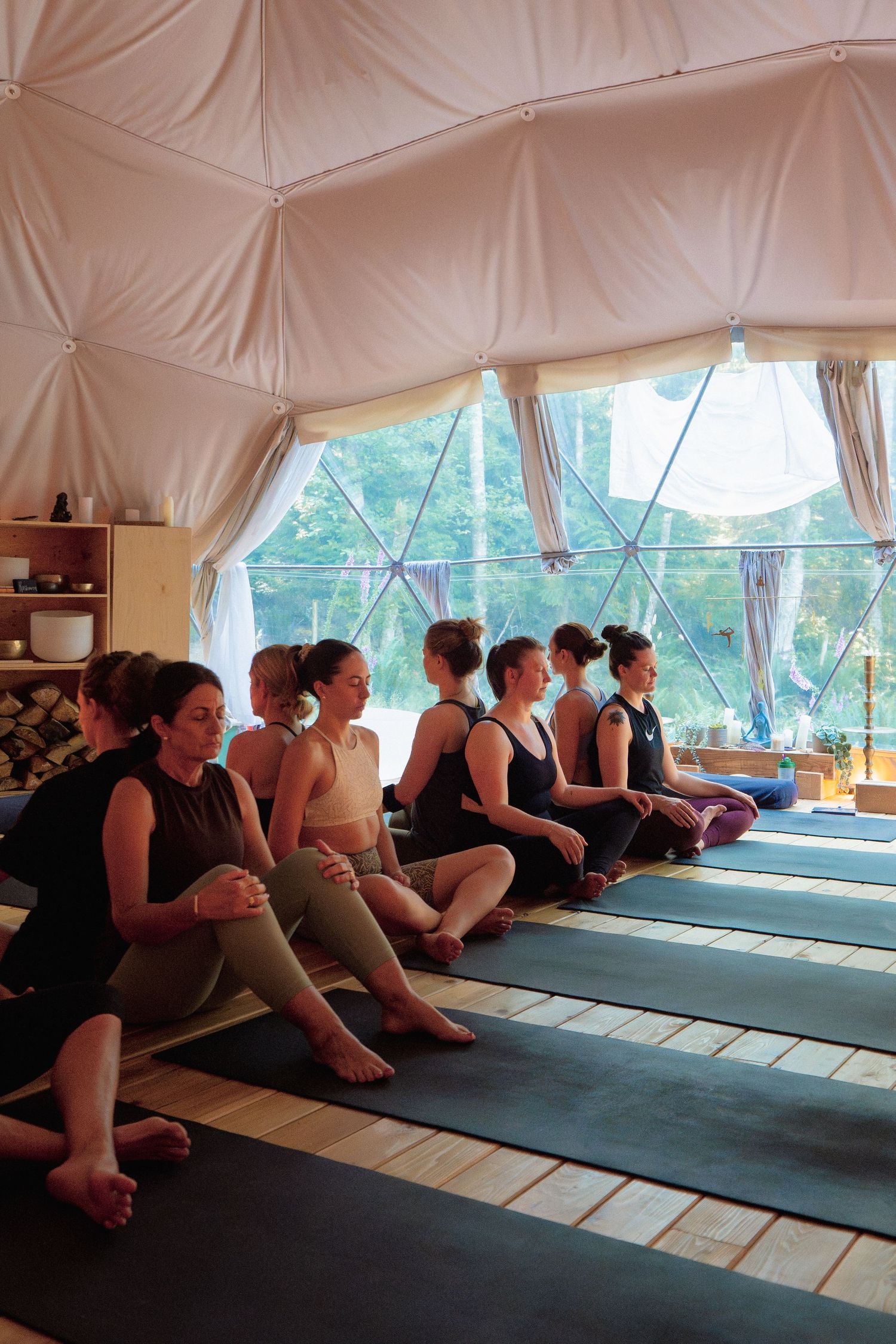 Students sit in meditation on yoga mats inside a light-filled dome studio.