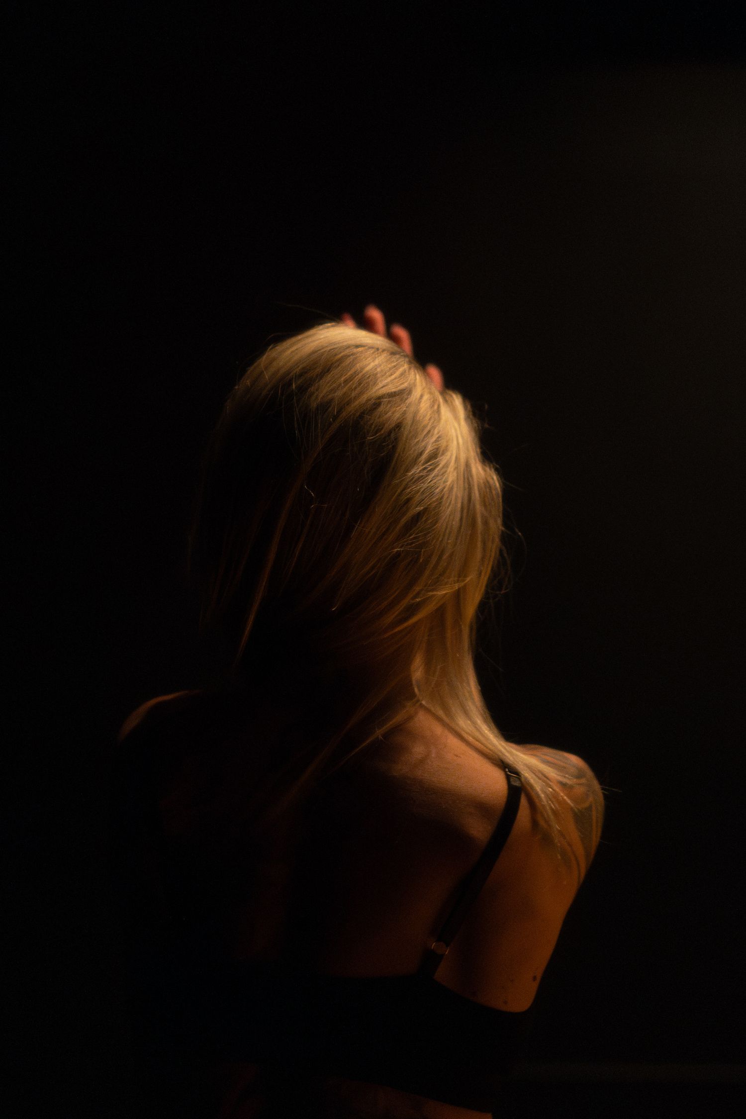 Back view portrait of blonde hair illuminated by dramatic low lighting against dark background.