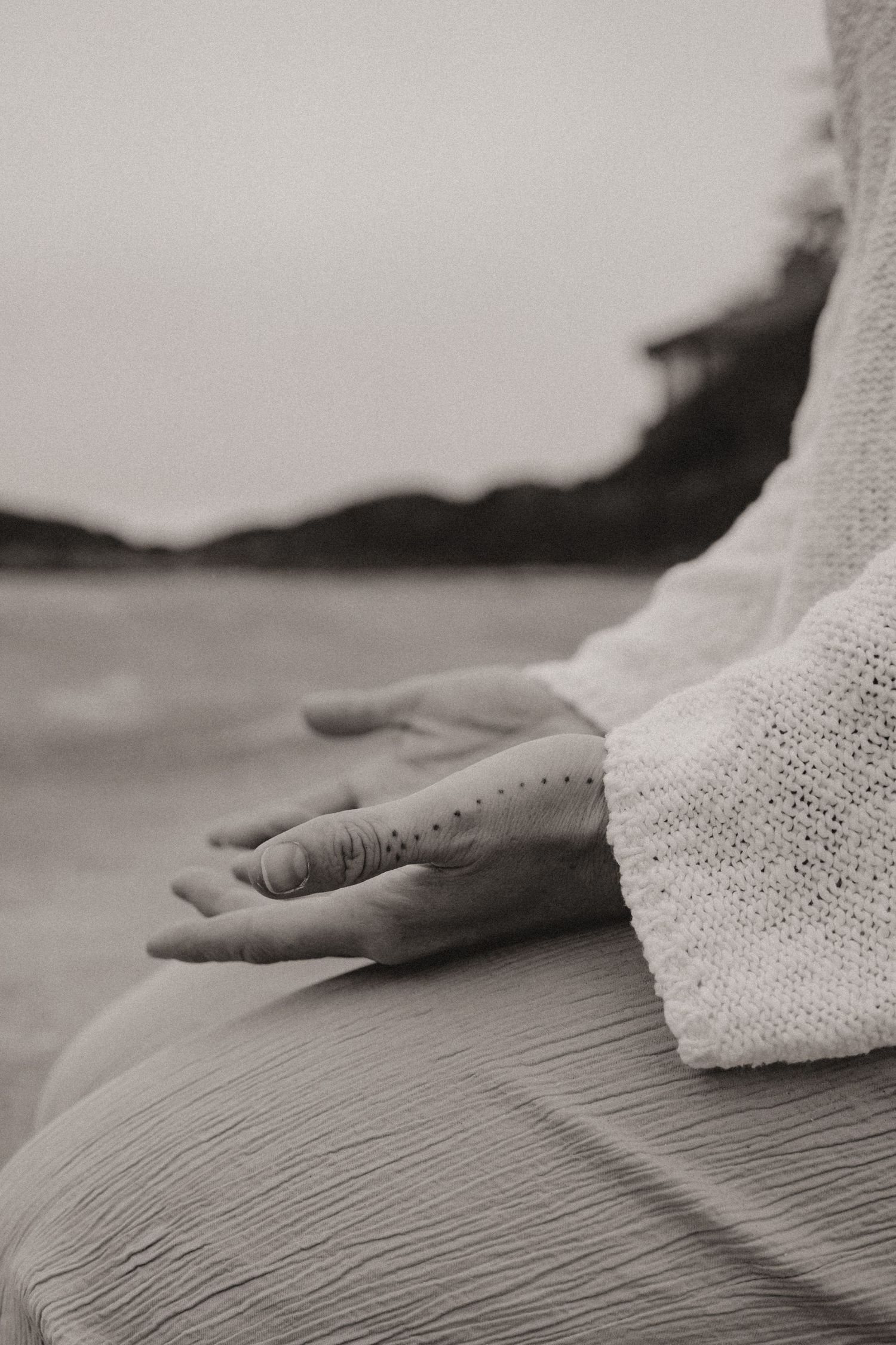 Close-up of hands resting on legs during meditation on a beach at sunset.