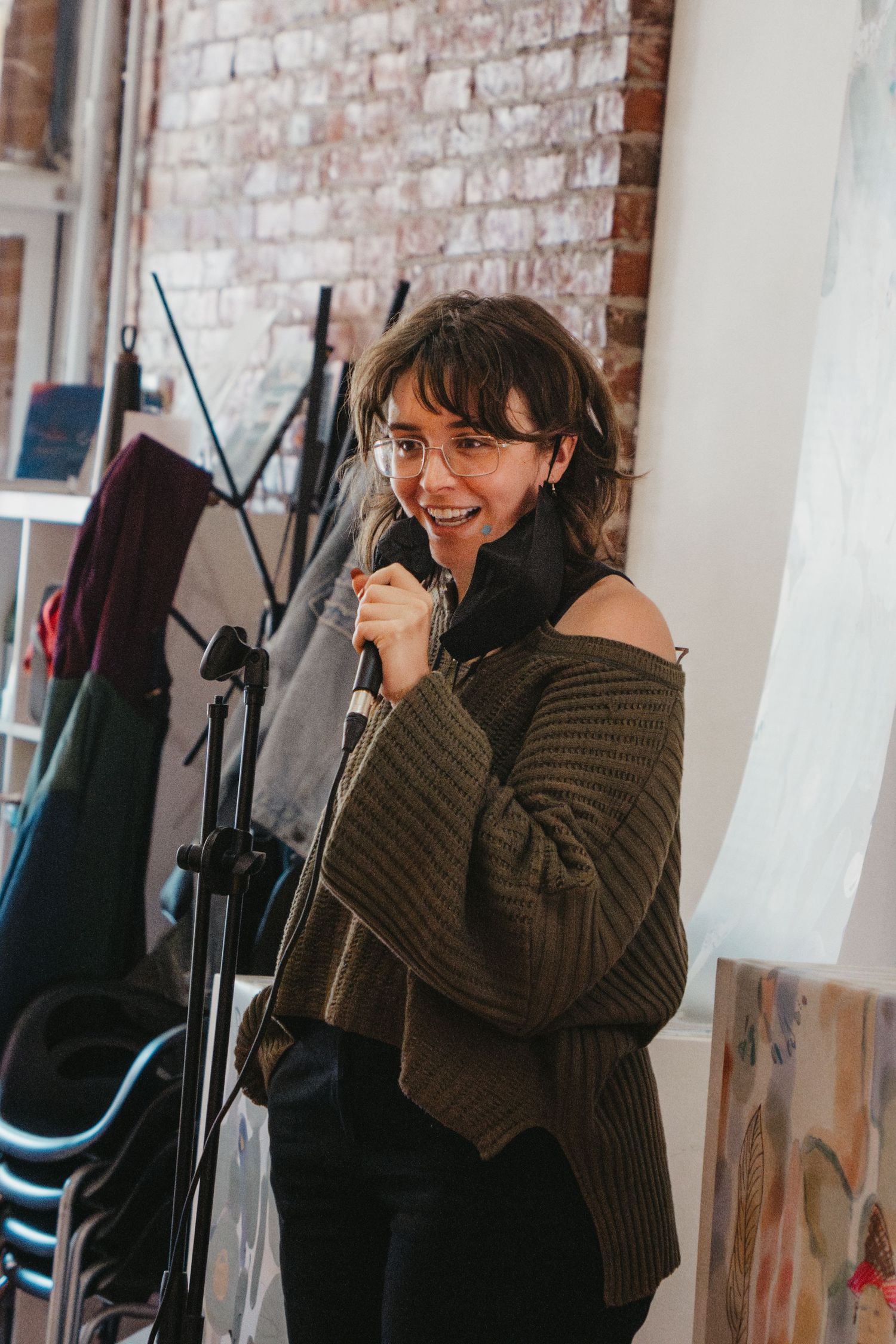 A performer speaks into a microphone at an indoor venue with exposed brick walls.