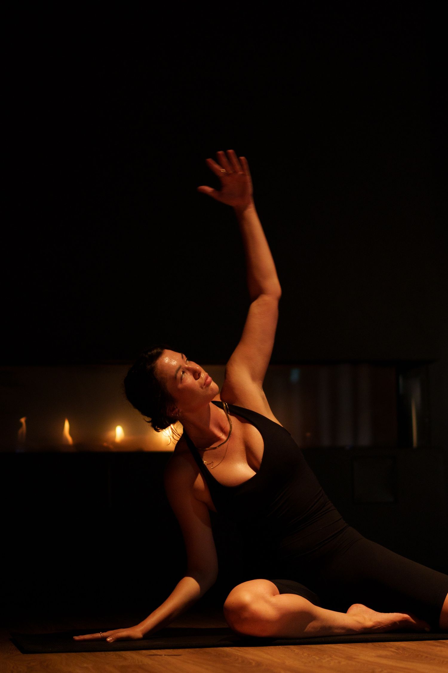 Dancer performs expressive floor movement by candlelight wearing black attire.