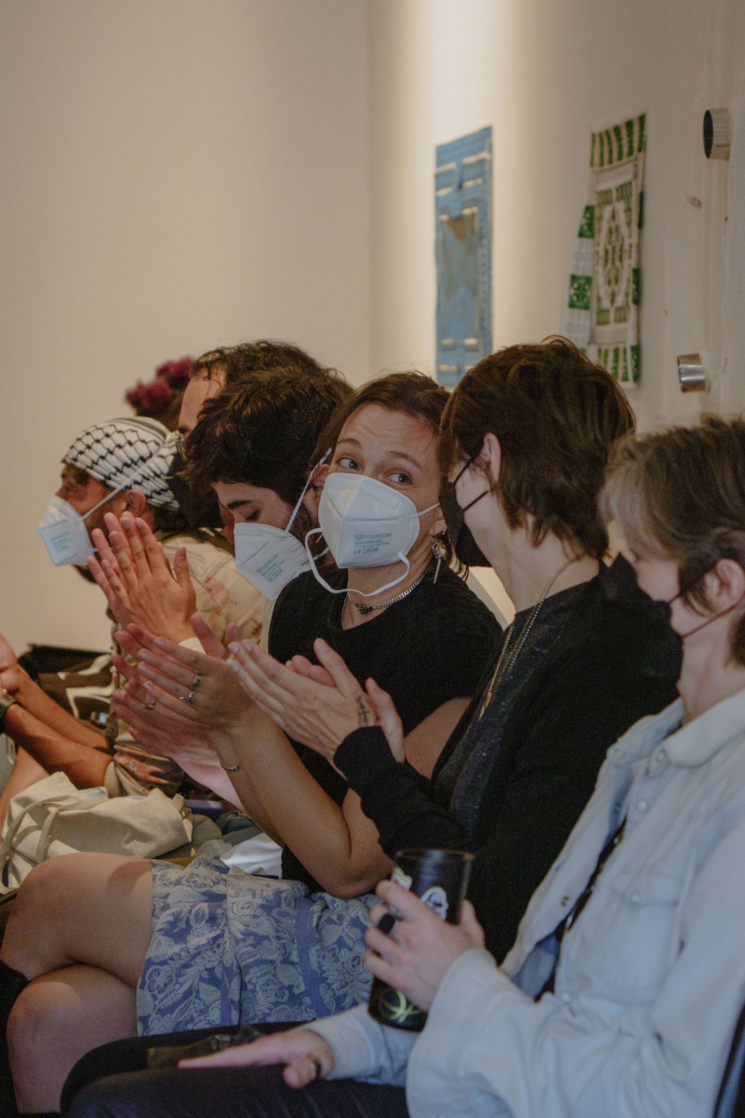 Masked audience members applaud during indoor presentation.