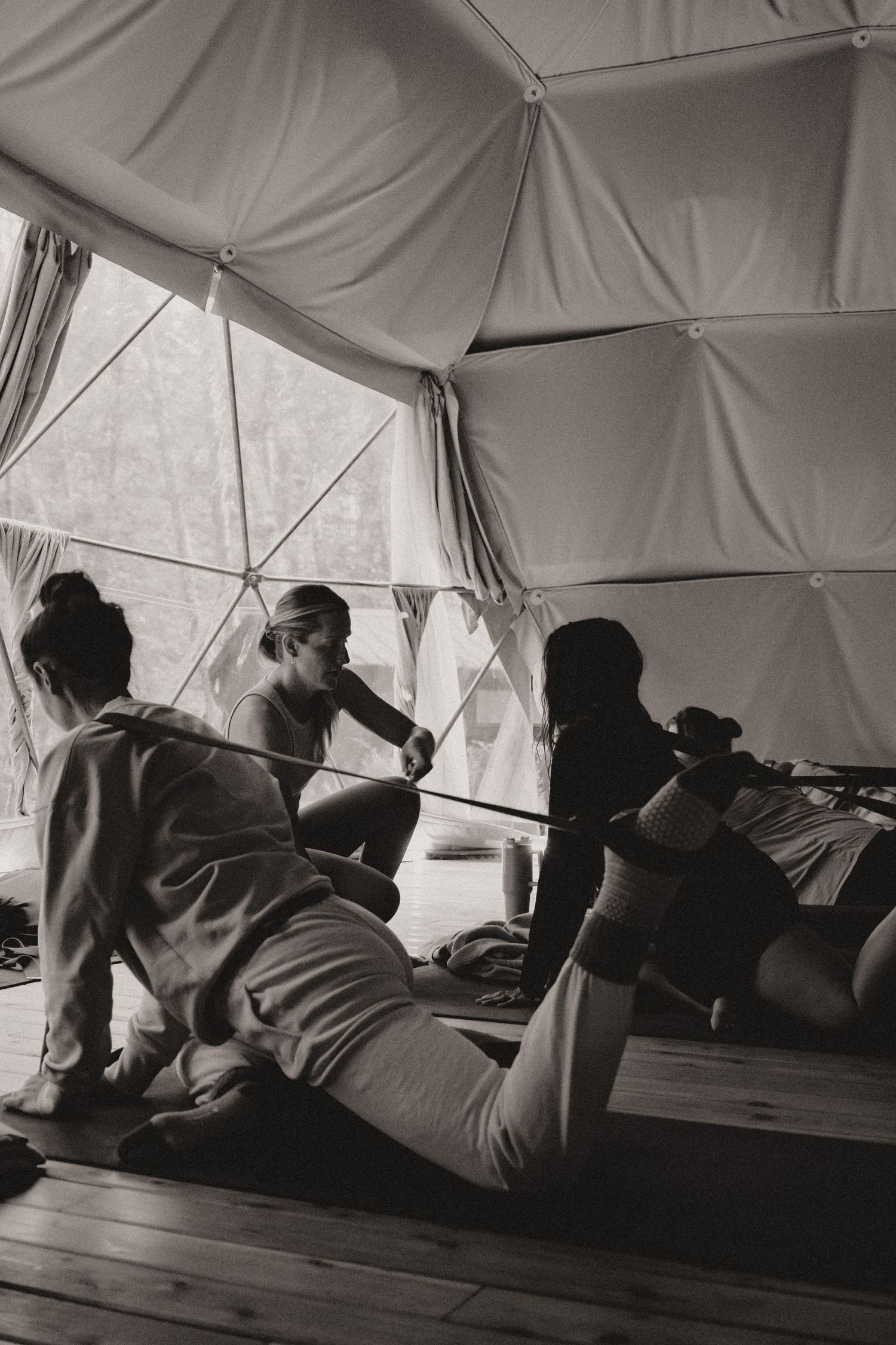 Wellness session participants practicing stretches on wooden floor in a dome tent.