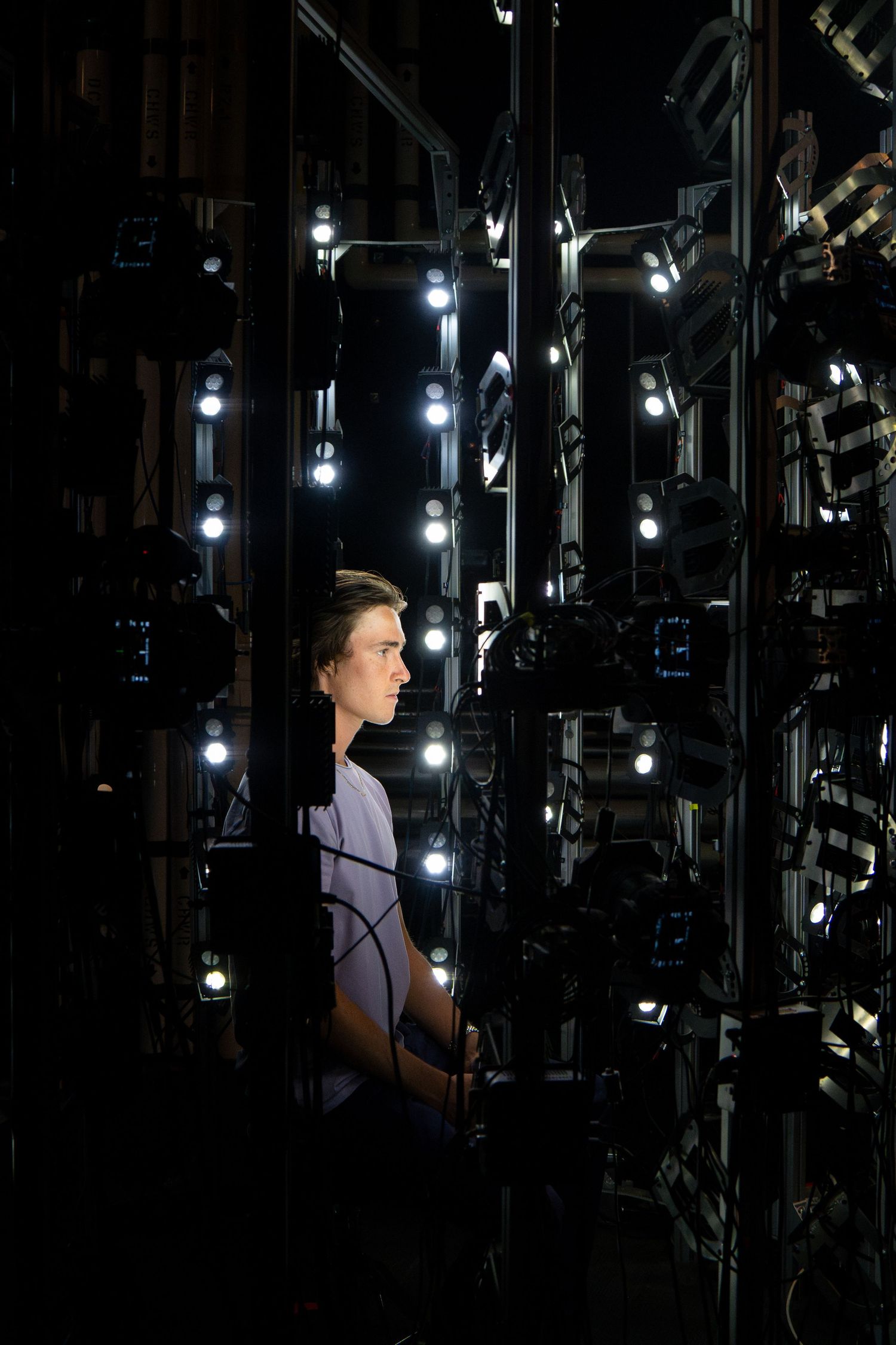 Person standing among dramatic lighting setup with multiple spotlights in dark studio setting.