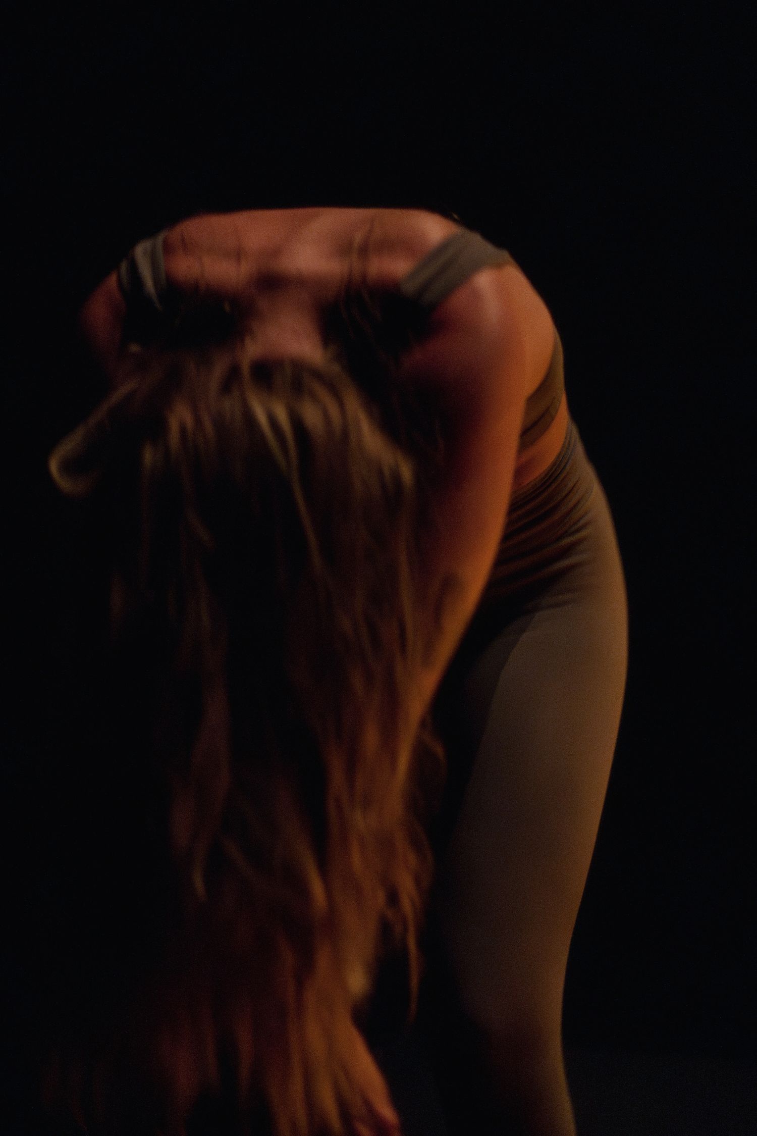 Silhouette of a dancer bending forward with flowing hair in warm atmospheric lighting.
