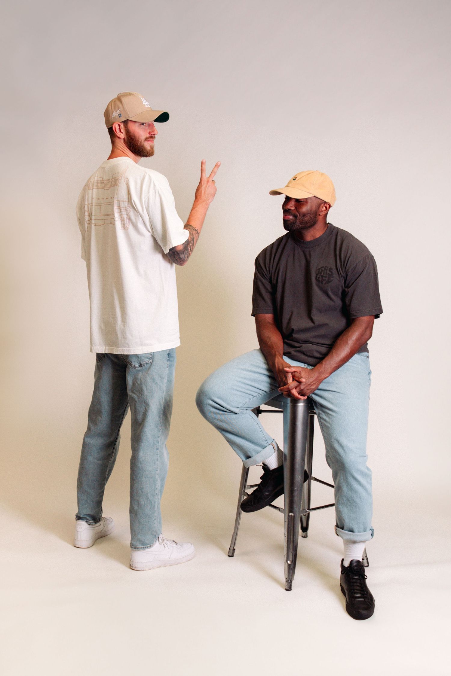 Two people in casual attire posing in studio against white background.