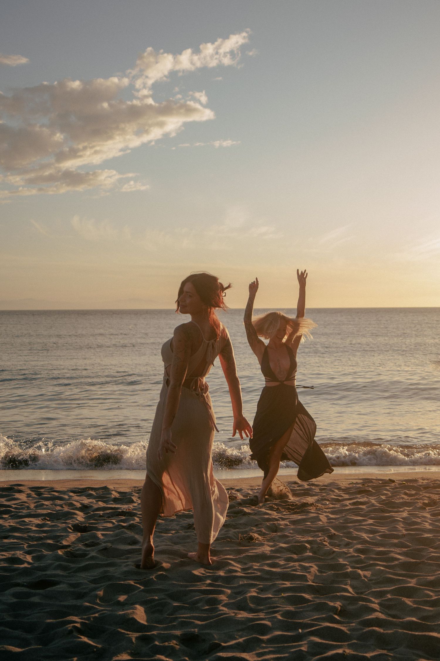 Silhouettes dance joyfully on a beach at sunset with waves crashing in the background.