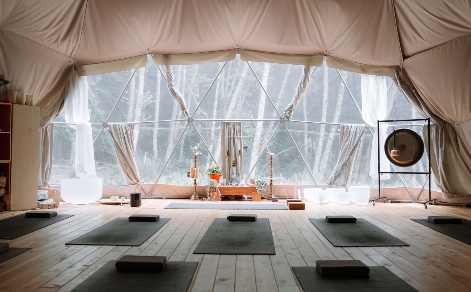 Serene yoga studio with black mats arranged on wooden floor in light-filled tent space.
