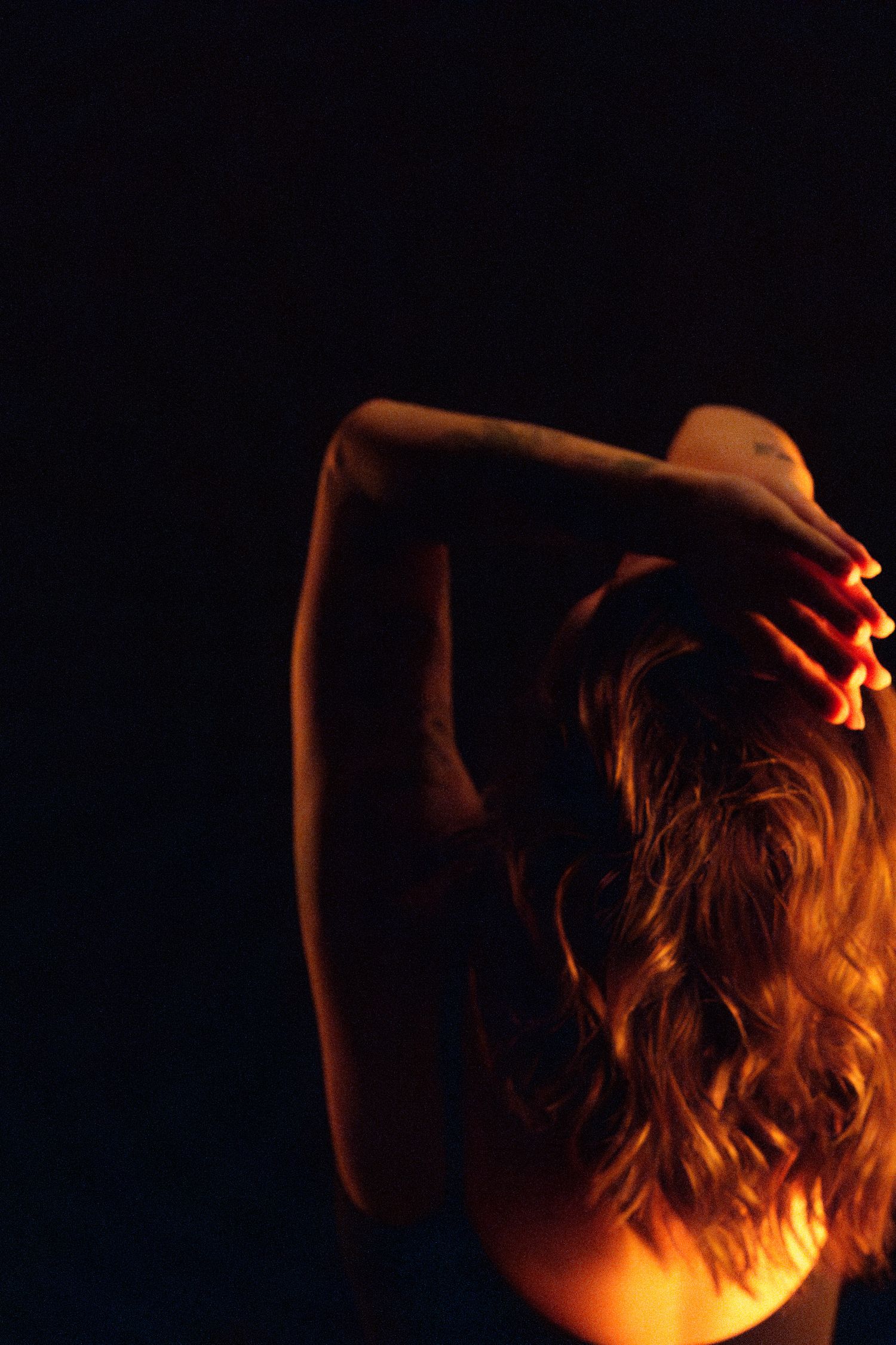 Dramatic backlit silhouette of a person with flowing hair in warm amber lighting against dark background.
