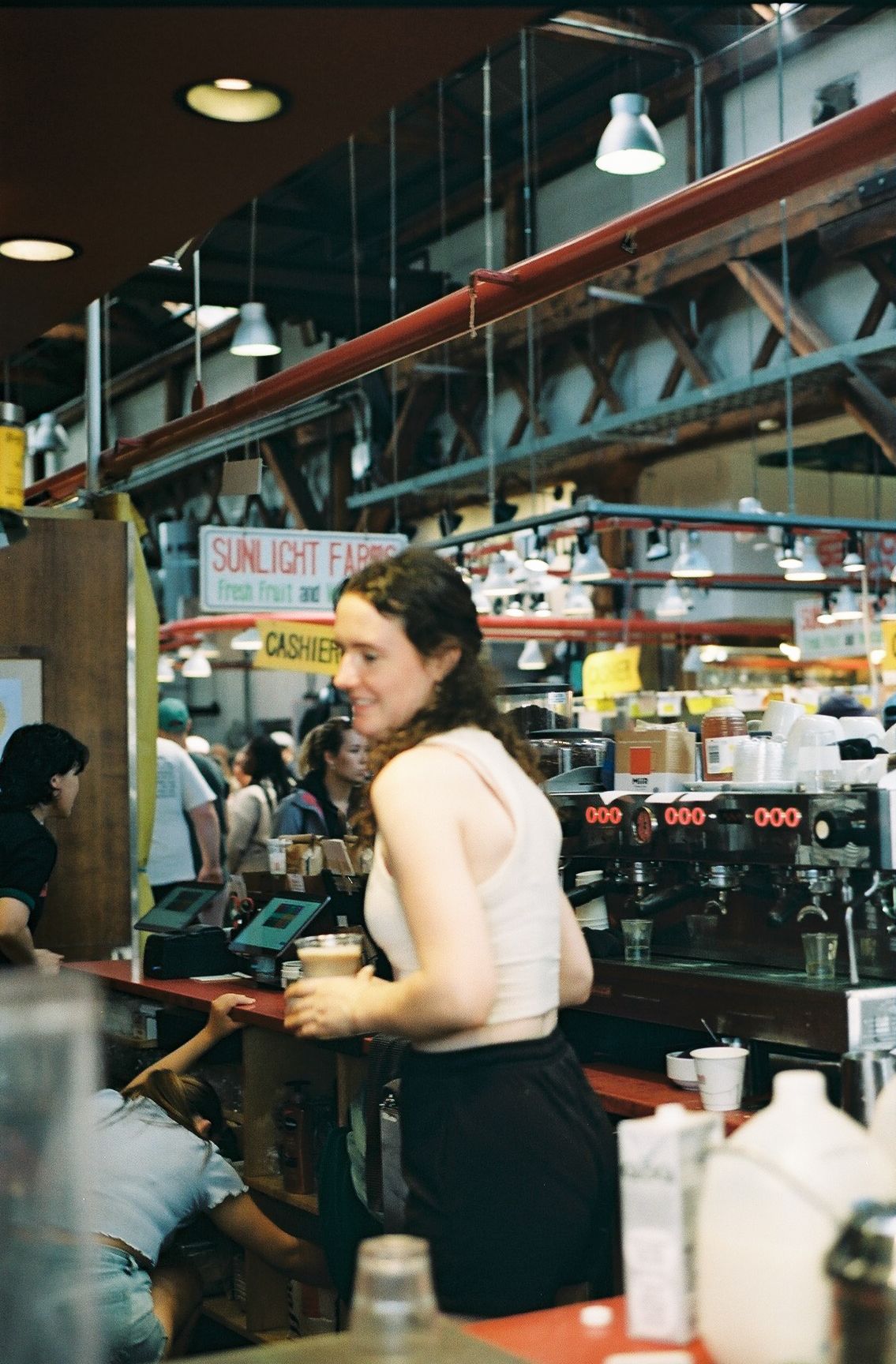 Barista taking orders at busy coffee shop counter with industrial decor.