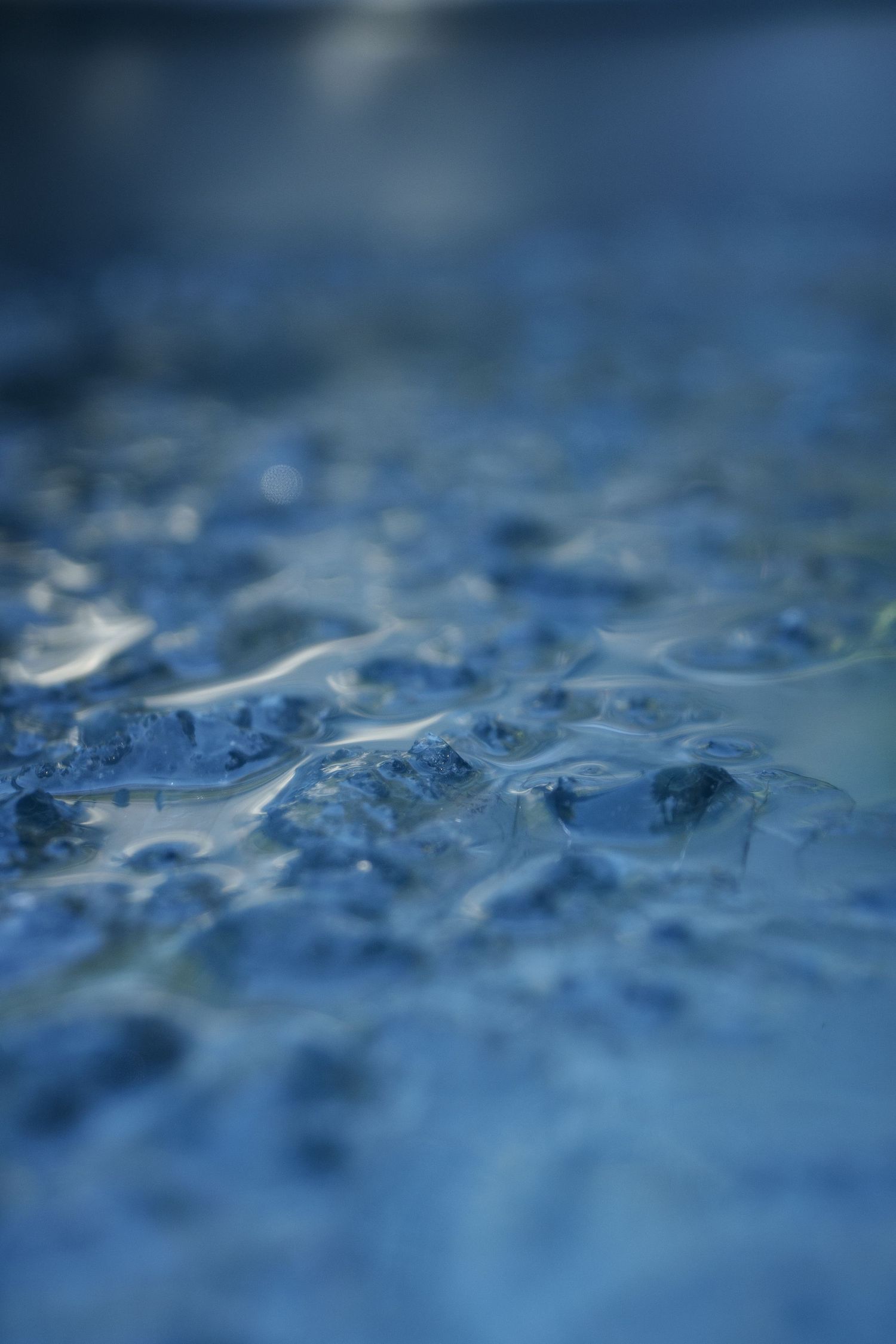 Abstract macro shot of blue rippling water surface with bokeh effects.