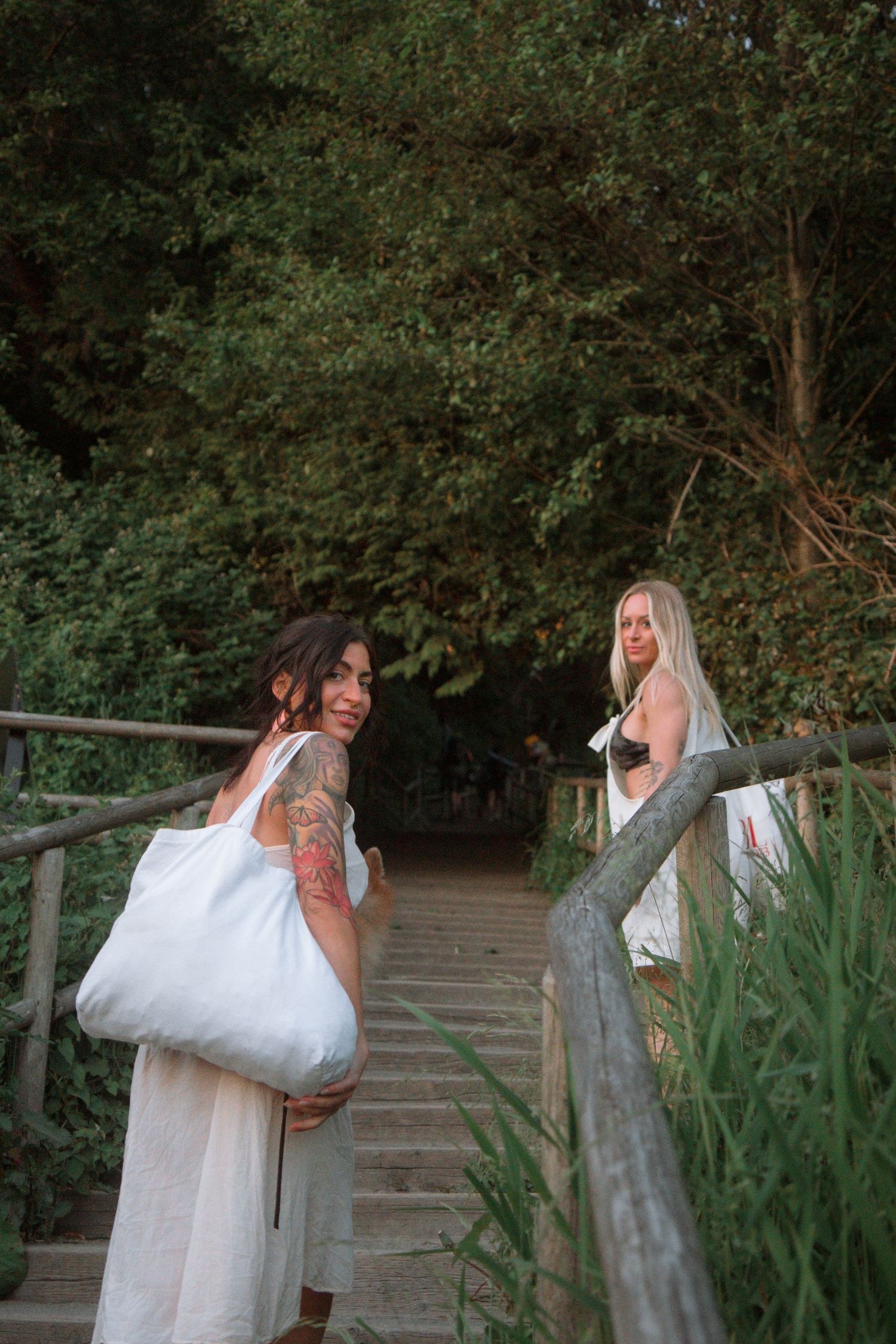 Two people carrying white bags ascending wooden stairs surrounded by greenery.