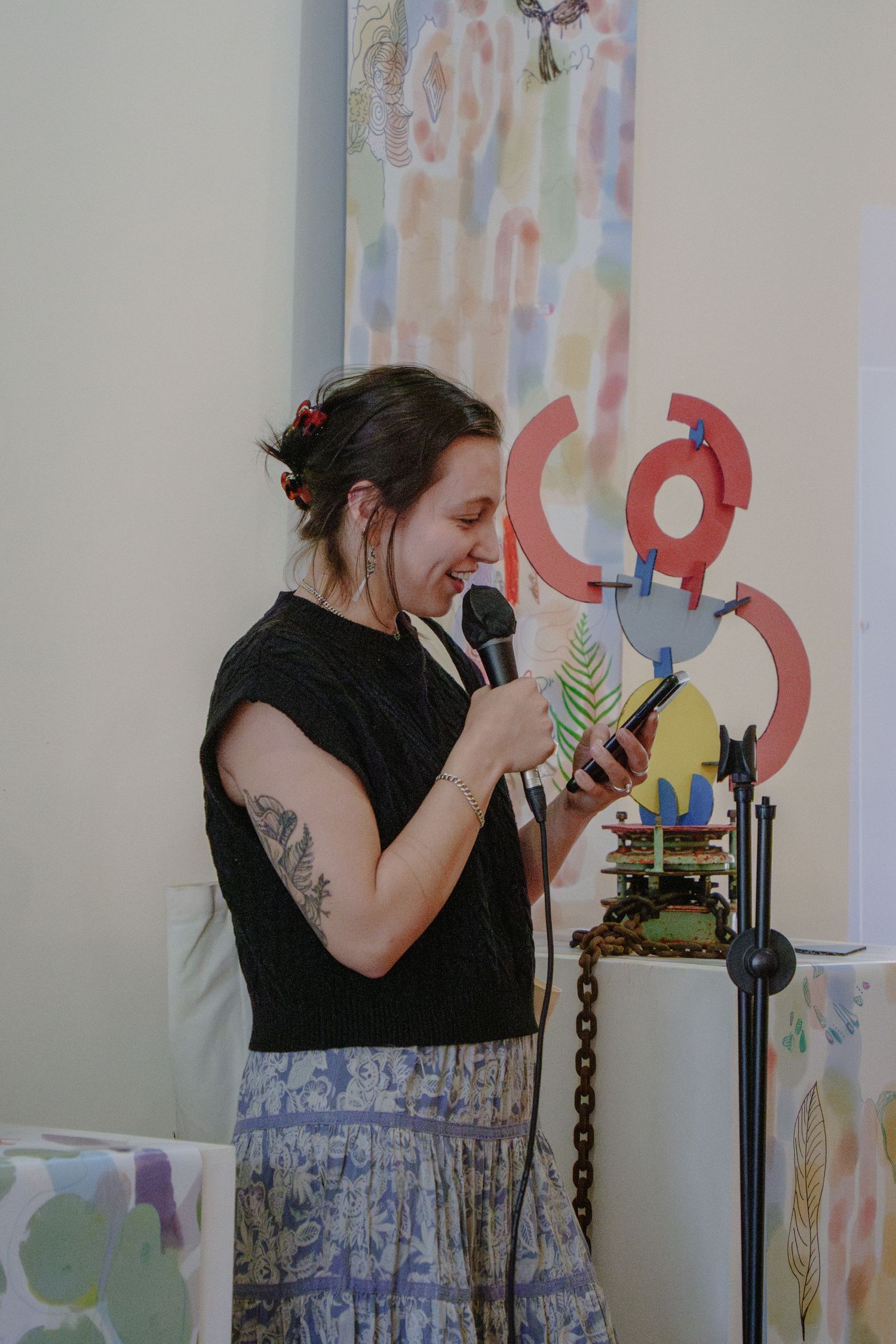 A performer speaks into a microphone against a colorful artistic wall display.