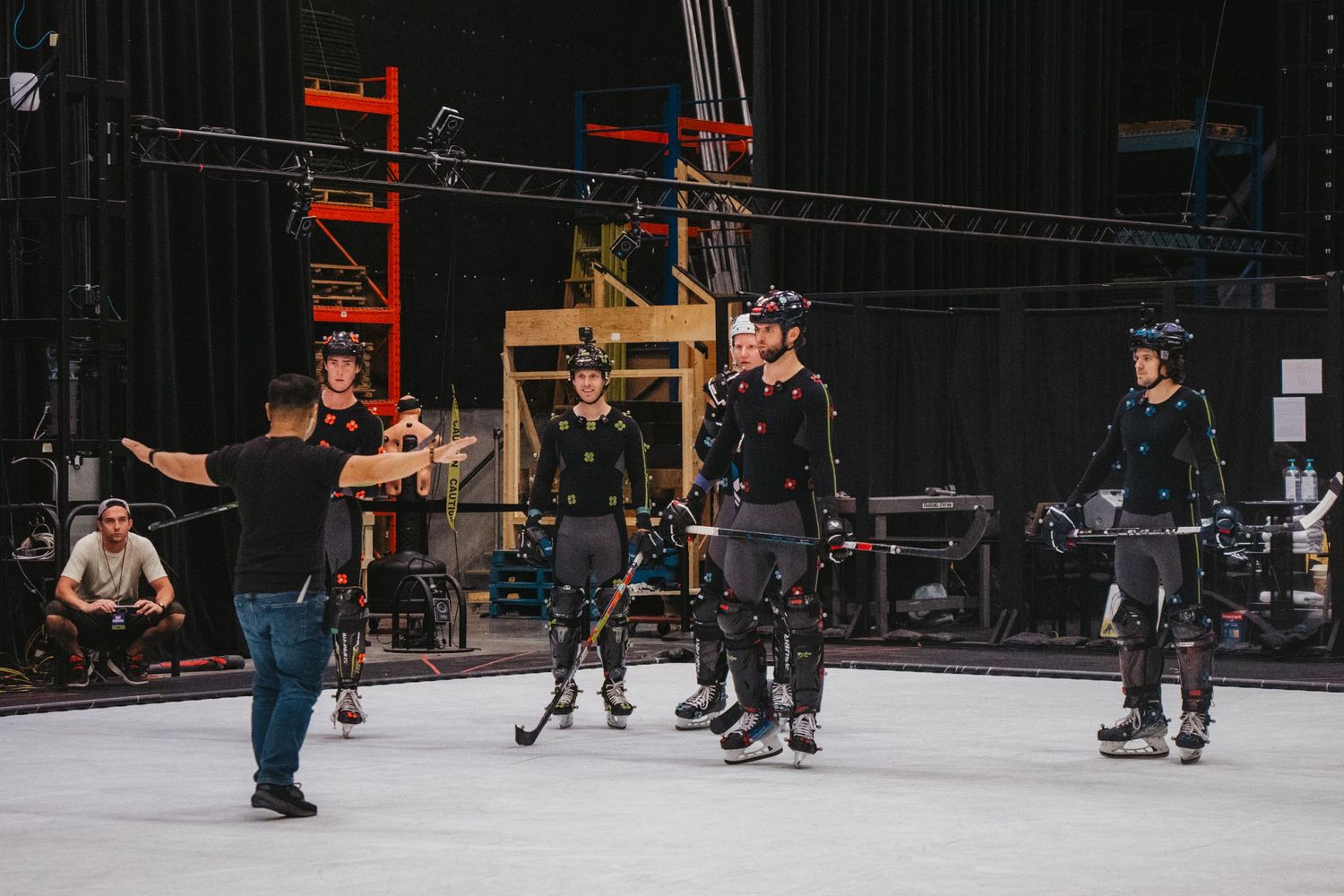 Motion capture performers in black suits rehearse on a soundstage with technical equipment visible.