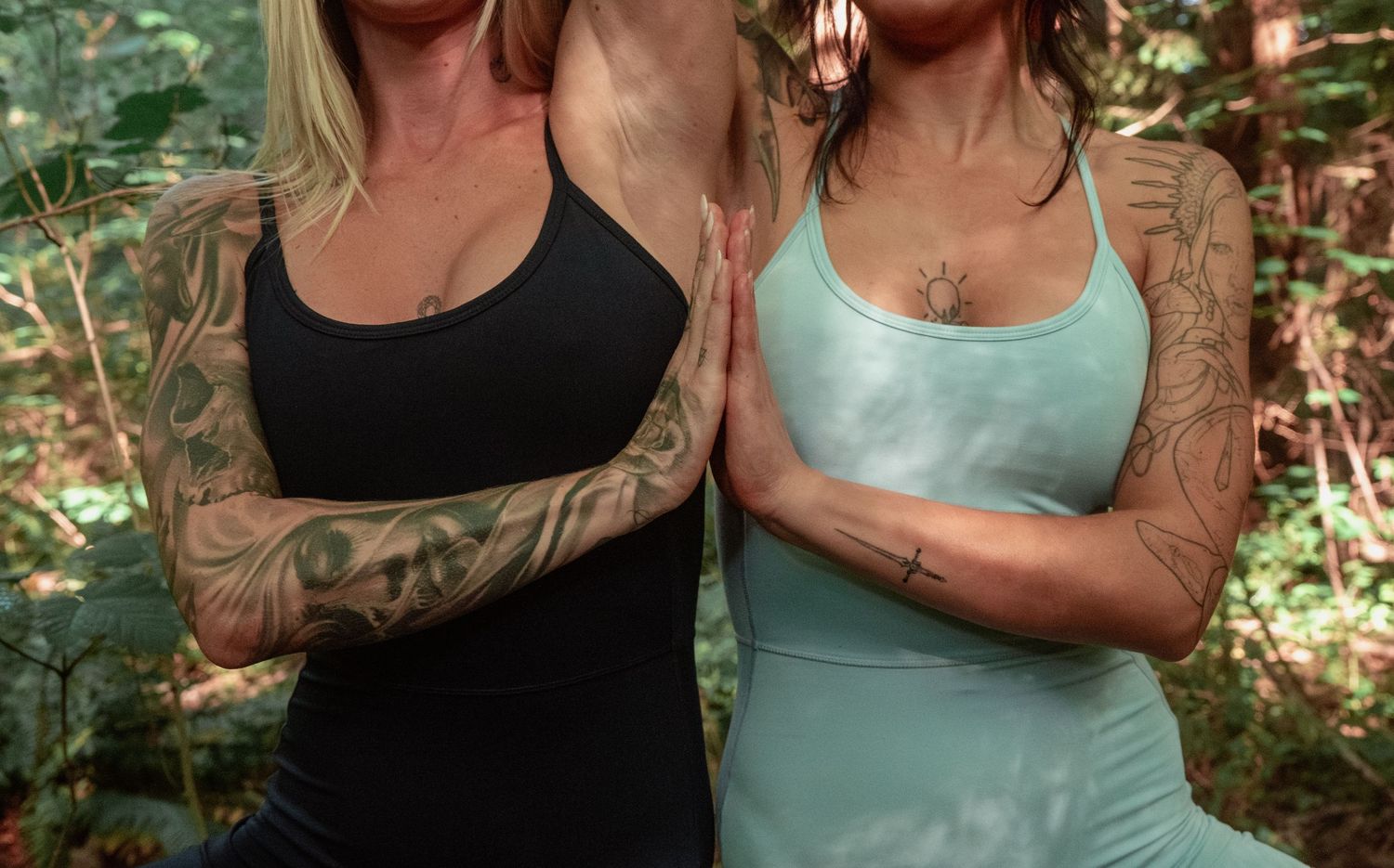 Close-up of two dancers showing tattooed arms while wearing black and mint colored athletic wear.