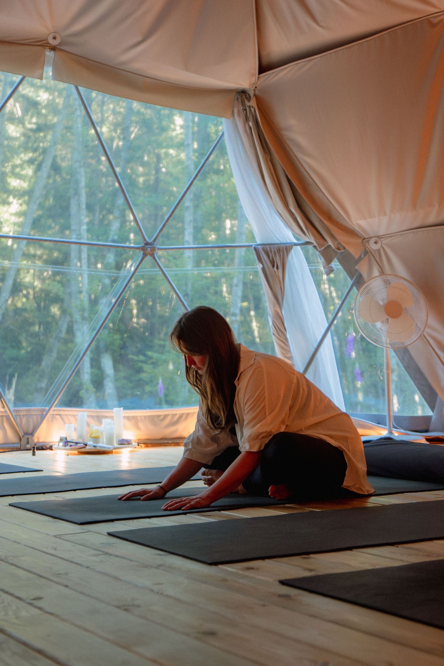 A yoga practitioner stretches on a mat inside a geodesic dome tent with natural light streaming through windows.