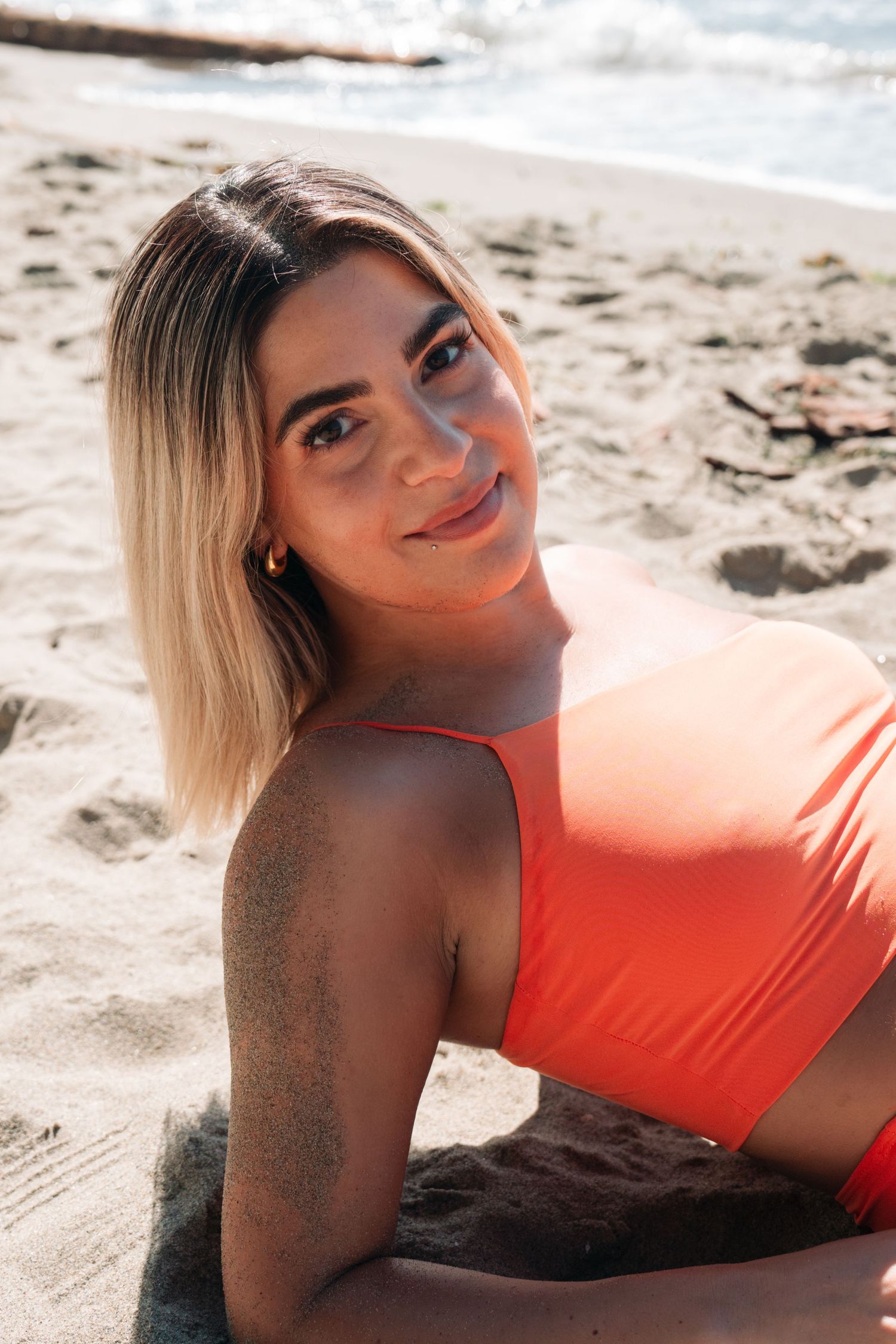 Woman in coral swimwear poses on sandy beach on sunny day.