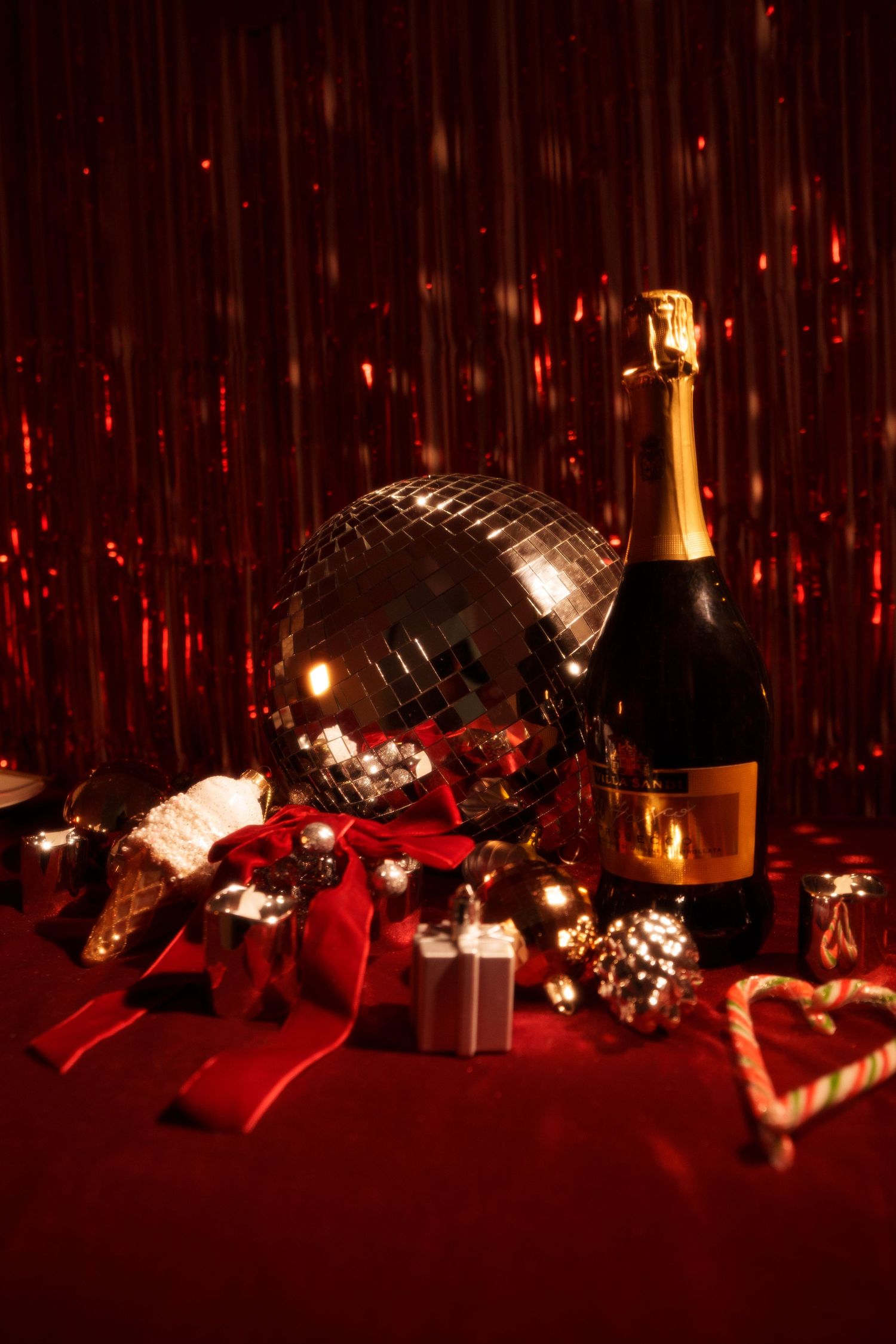 Festive holiday setup with disco ball, champagne bottle, and wrapped gifts on red background.