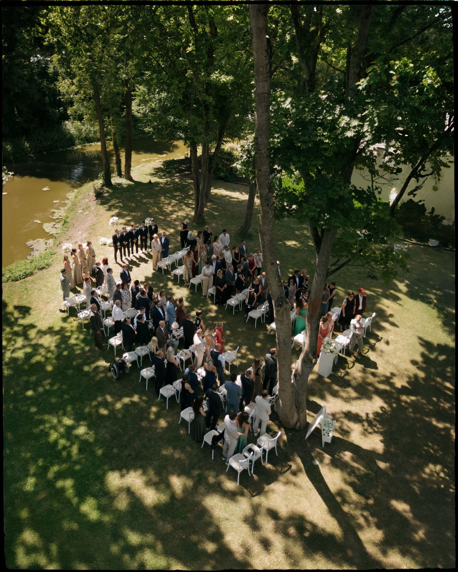 An outdoor wedding ceremony in a lush forest setting viewed from multiple aerial angles showing guests seated in white chairs.