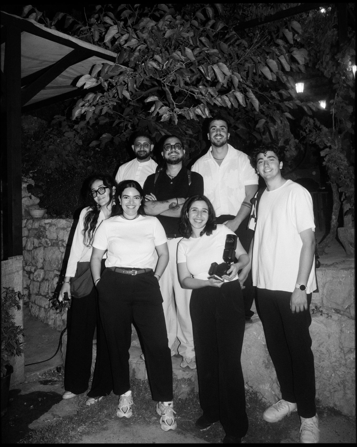 Black and white photo sequence of a group posing together in casual attire during a nighttime outdoor gathering.