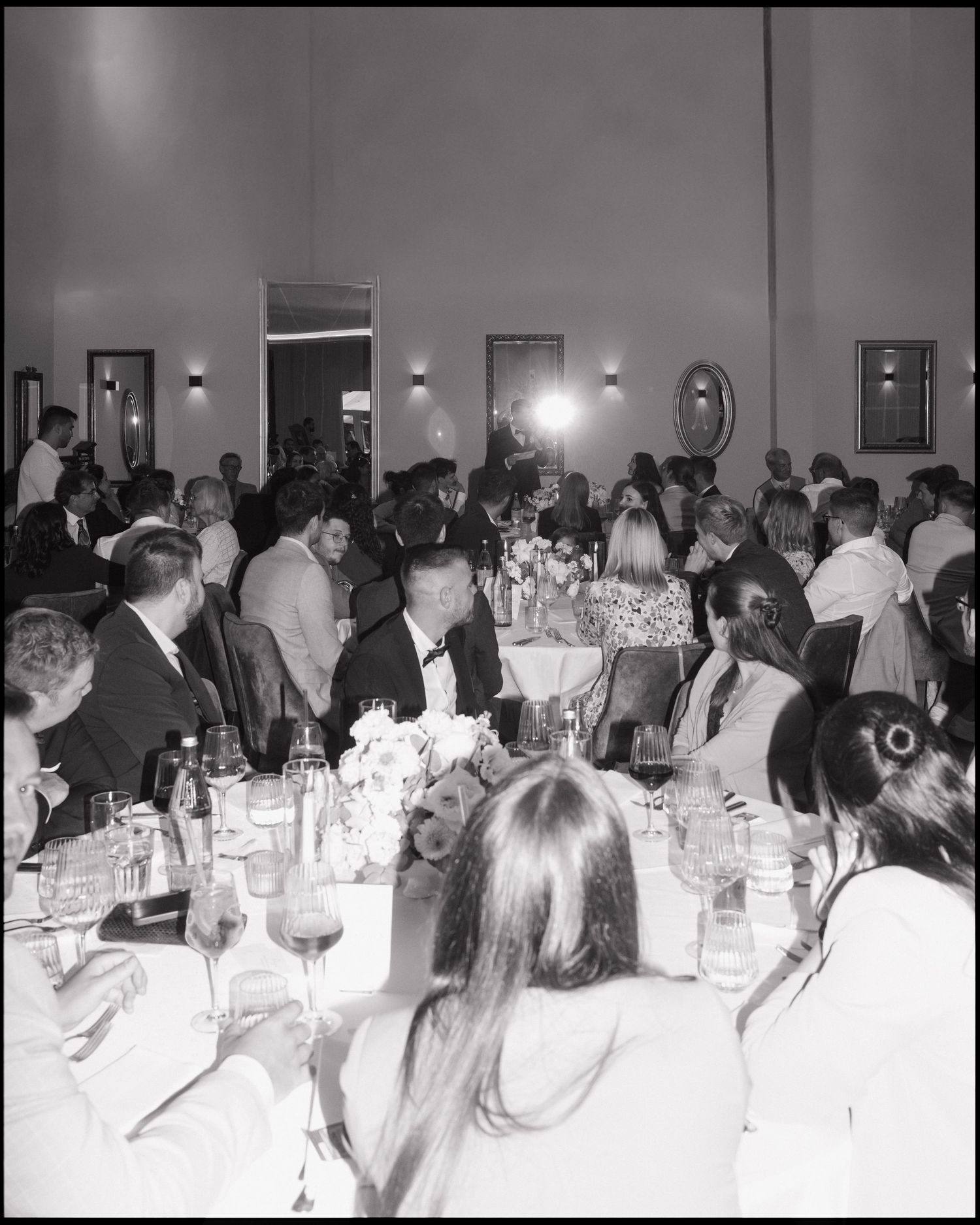 A black and white photograph shows a crowded formal dinner event with guests seated at tables in a banquet hall.