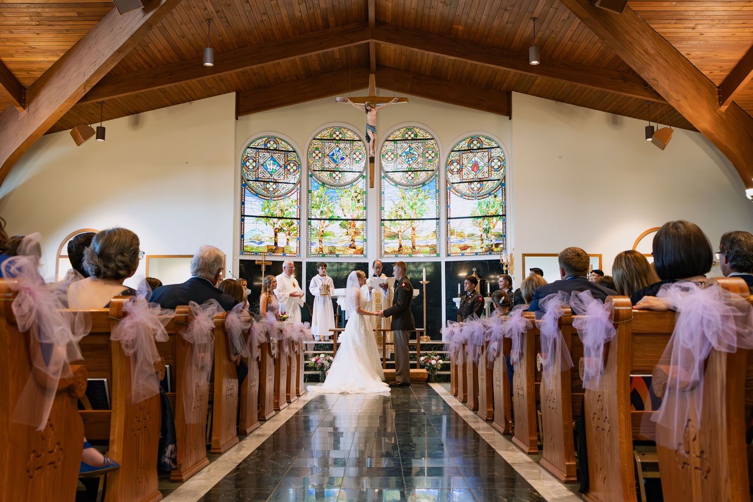 Interior view of a church sanctuary with wooden beams and stained glass windows decorated with white bows on the pews.