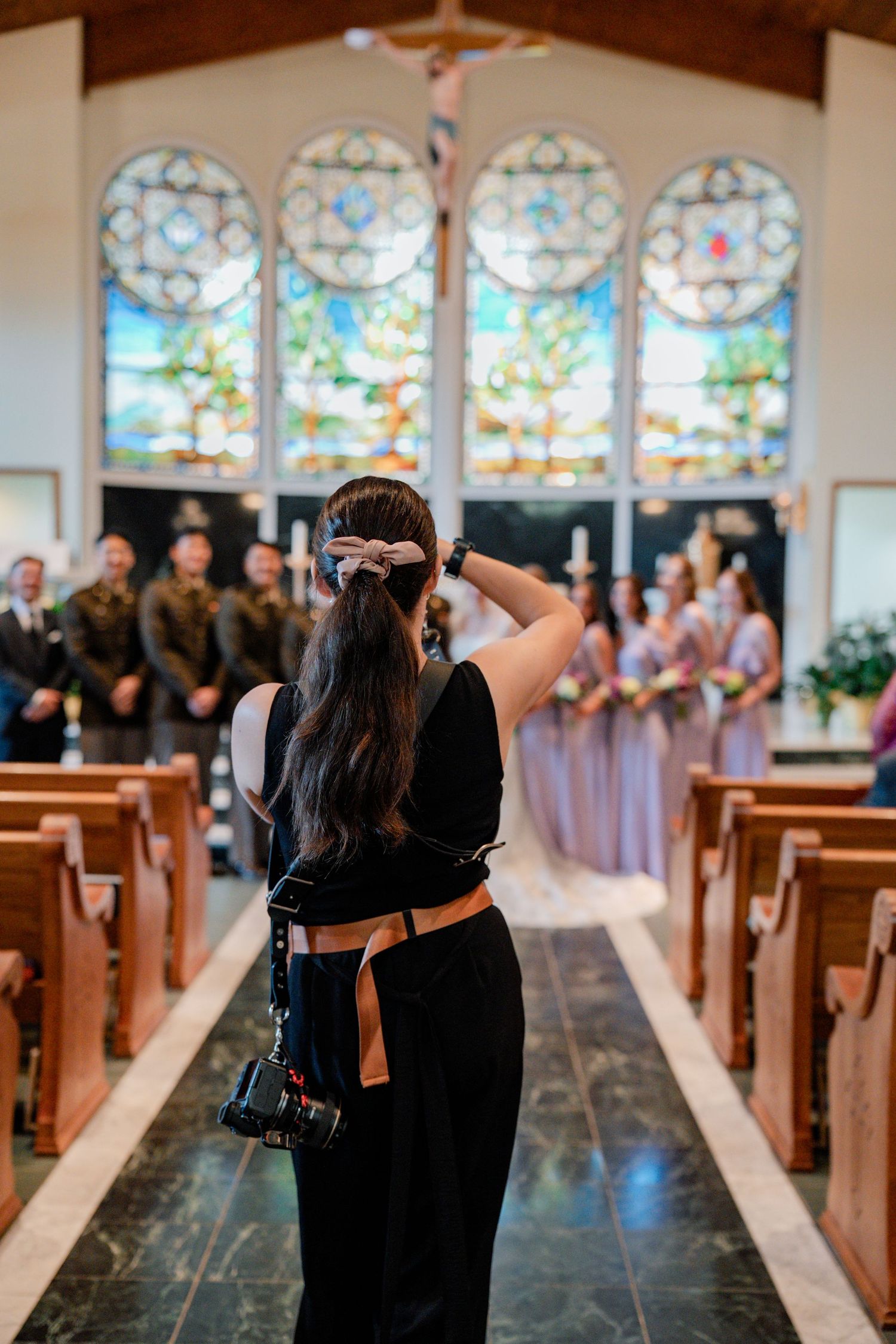 Row of stained glass windows and wooden pews in a church sanctuary during a wedding ceremony.